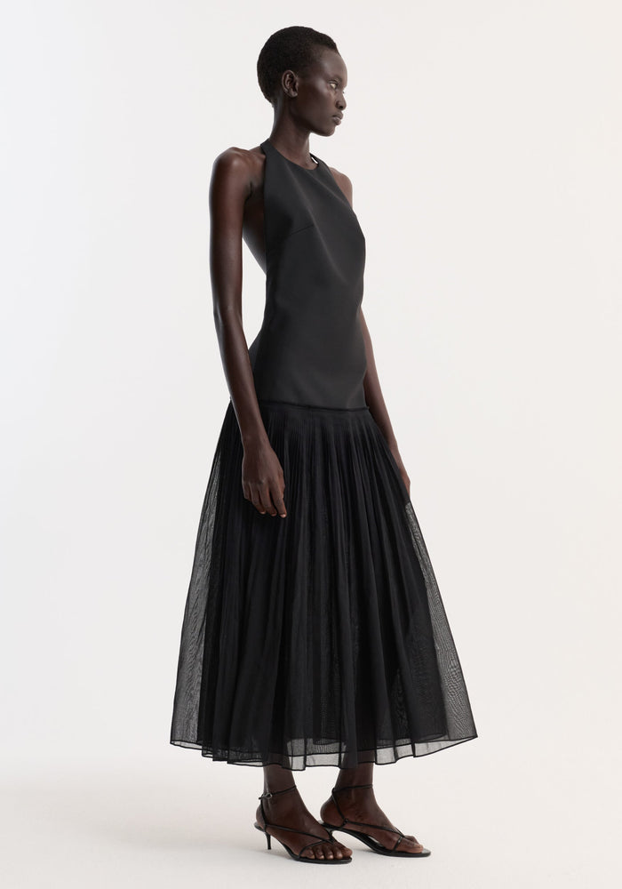 Model wearing the Pleated muslin halter dress | black, featuring a sleeveless, fitted bodice and full-length pleated skirt, styled with black strappy kitten-heel sandals.