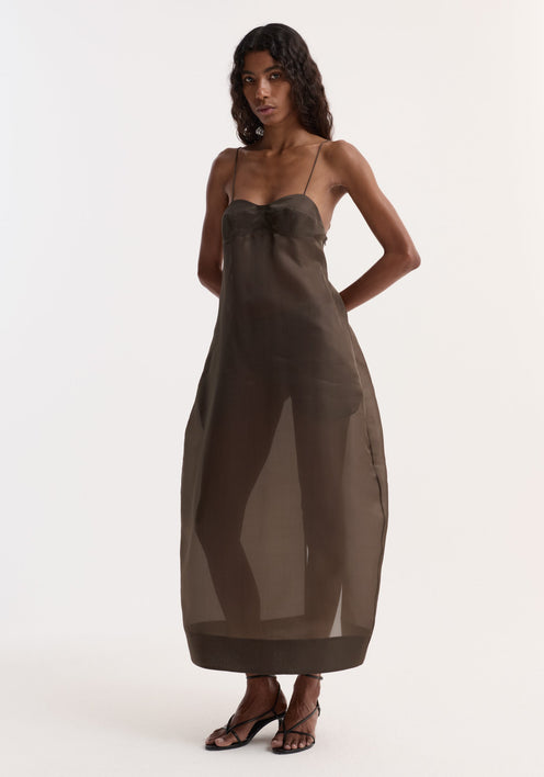 Sheer bustier volume dress | earth, featuring a sheer silk organza design with bustier detailing, adjustable straps, and a full sculptural skirt. Model wears black strappy sandals.