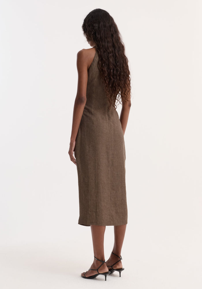 Sarong dress | brown melange: Woman in sleeveless, calf-length, linen dress with high neckline and sarong-inspired waist knot, paired with black strappy sandals.