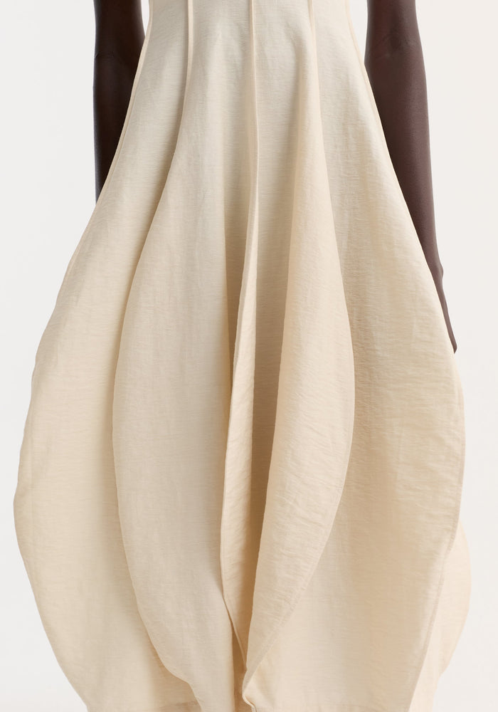 Open back tulip dress in butter showcases a balloon-hem skirt with petal-like pleats, halter neckline, and low back, crafted from silk-linen blend.