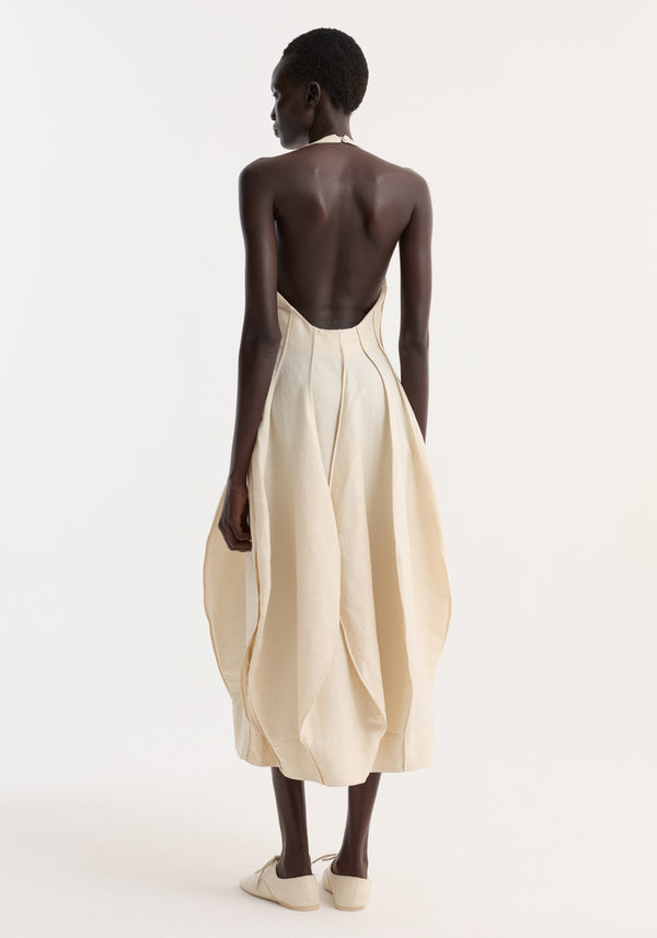 Model in Open Back Tulip Dress | Butter, showcasing its halter tie, open back, and pleated balloon skirt. The dress blends elegance with a sculptural silhouette.