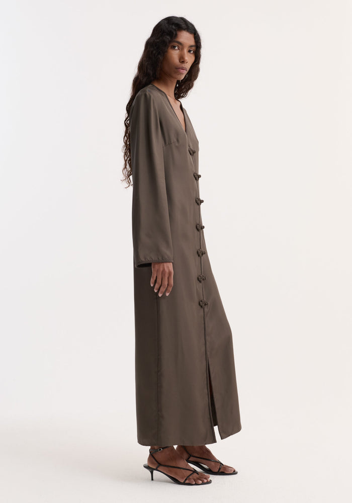 Model in profile wearing Pankou closure silk dress | earth, featuring long sleeves, V-neck, frog closures, and a front slit. Strappy sandals complete the look.