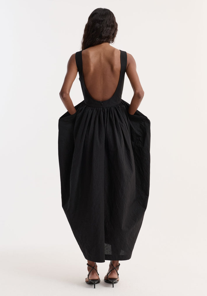 Model in Sculptural textured cotton dress | black, showcasing a sleeveless design with a deep scoop back, gathered voluminous skirt, and strappy heeled sandals.