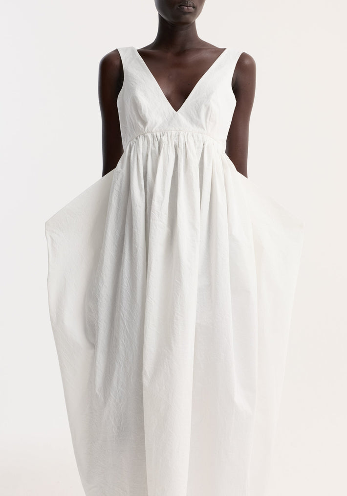 Sculptural textured cotton dress in off white, featuring a deep V-neck, empire waist, voluminous trapezium-shaped skirt, and wide shoulder straps.