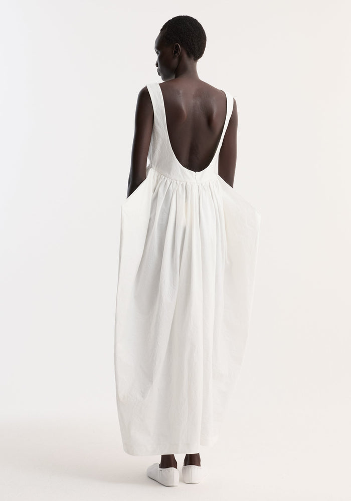 Sculptural textured cotton dress in off white, featuring a sleeveless design, v-neck, low scooped back, floor-length trapezium skirt, and side pockets.