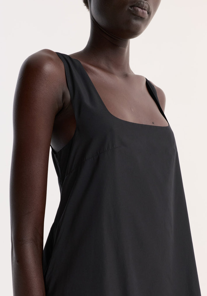 Close-up of a person wearing a Technical volume dress in black, highlighting its sleeveless design, square neckline, and draped fit with a distinctive balloon hemline.