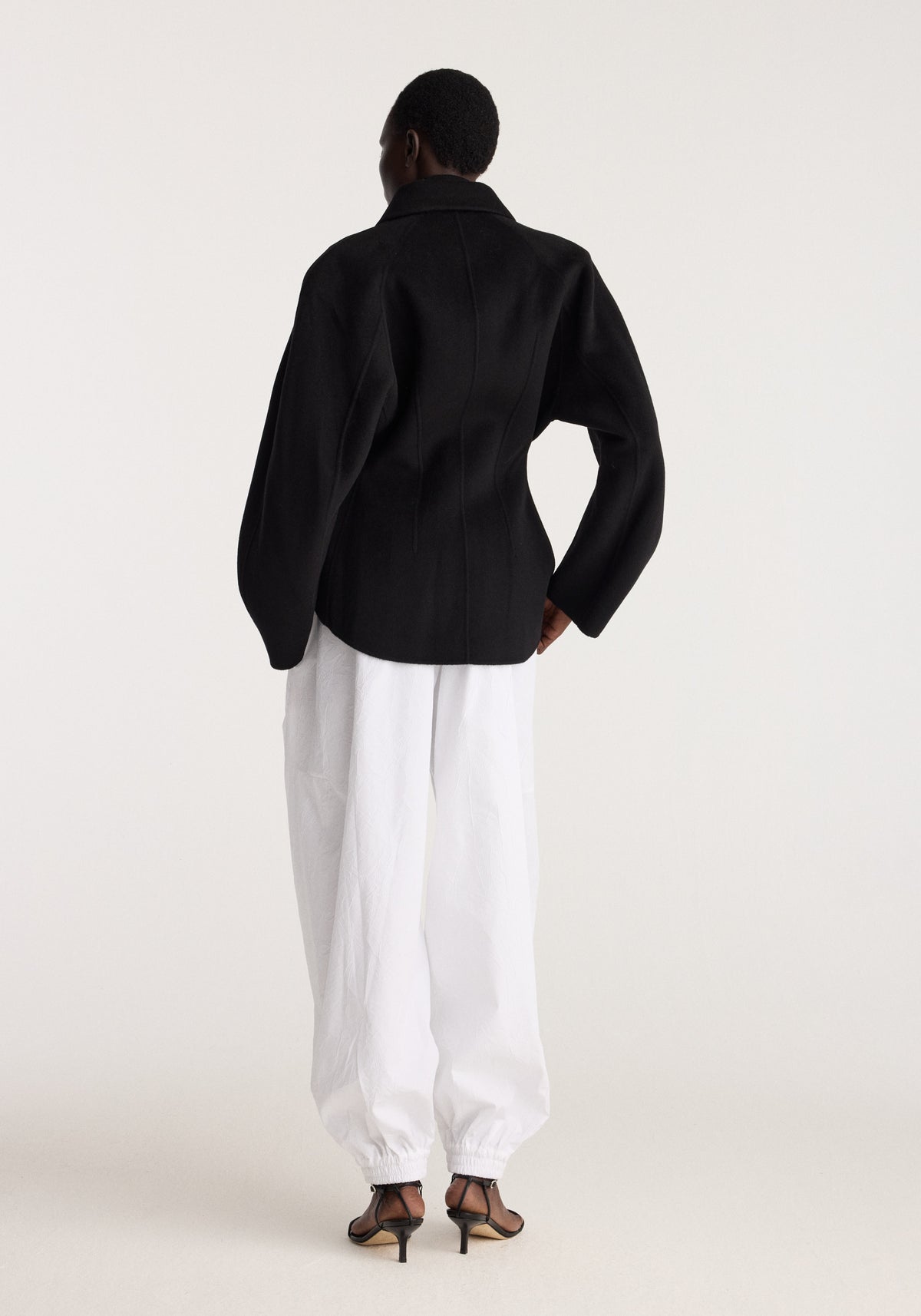 Double-faced sculptural jacket | black shown from the back on a model with voluminous sleeves worn with white trousers and heeled sandals