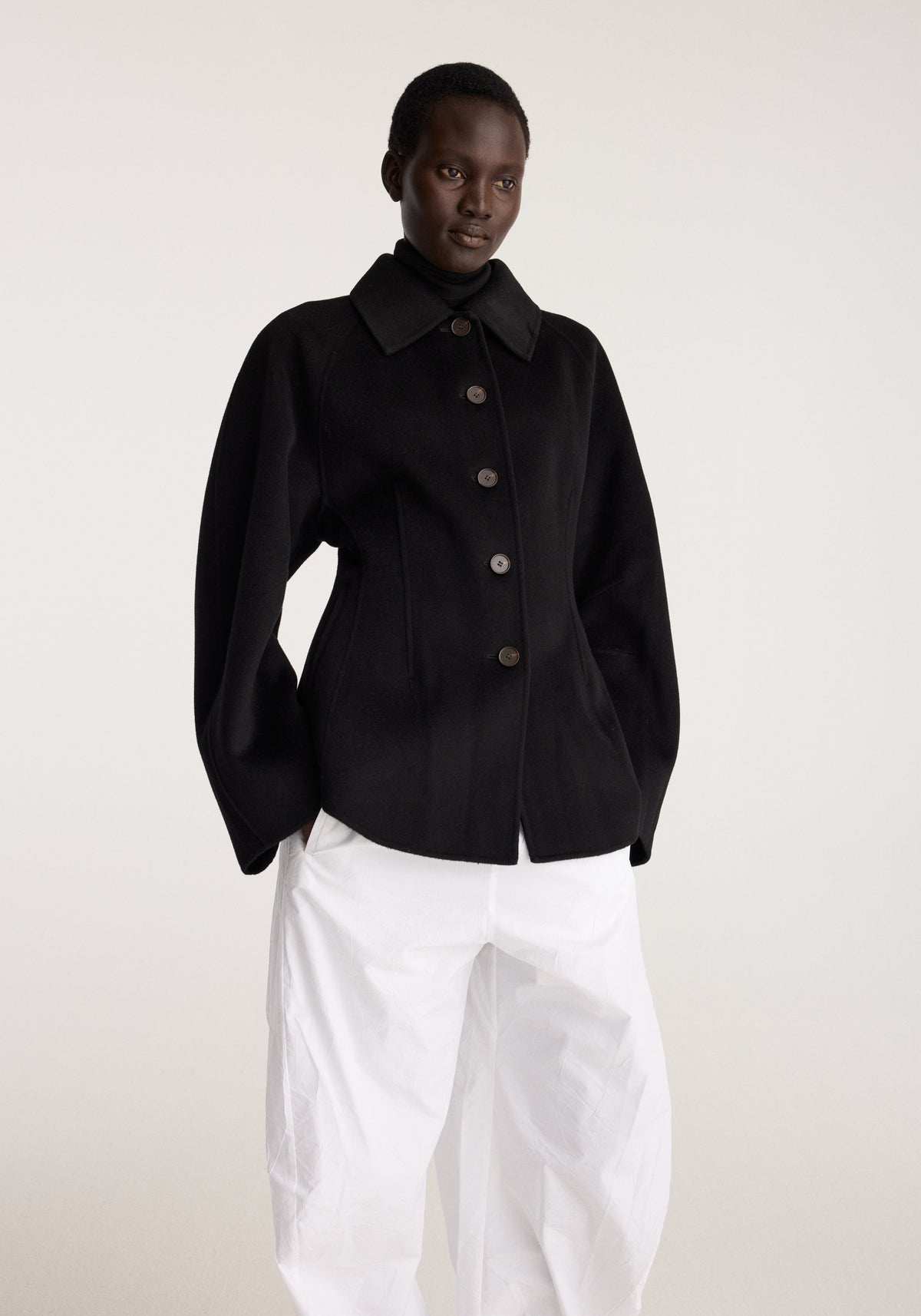 Double-faced sculptural jacket | black worn by a model with a structured collar and button front styled with relaxed white trousers against a neutral backdrop