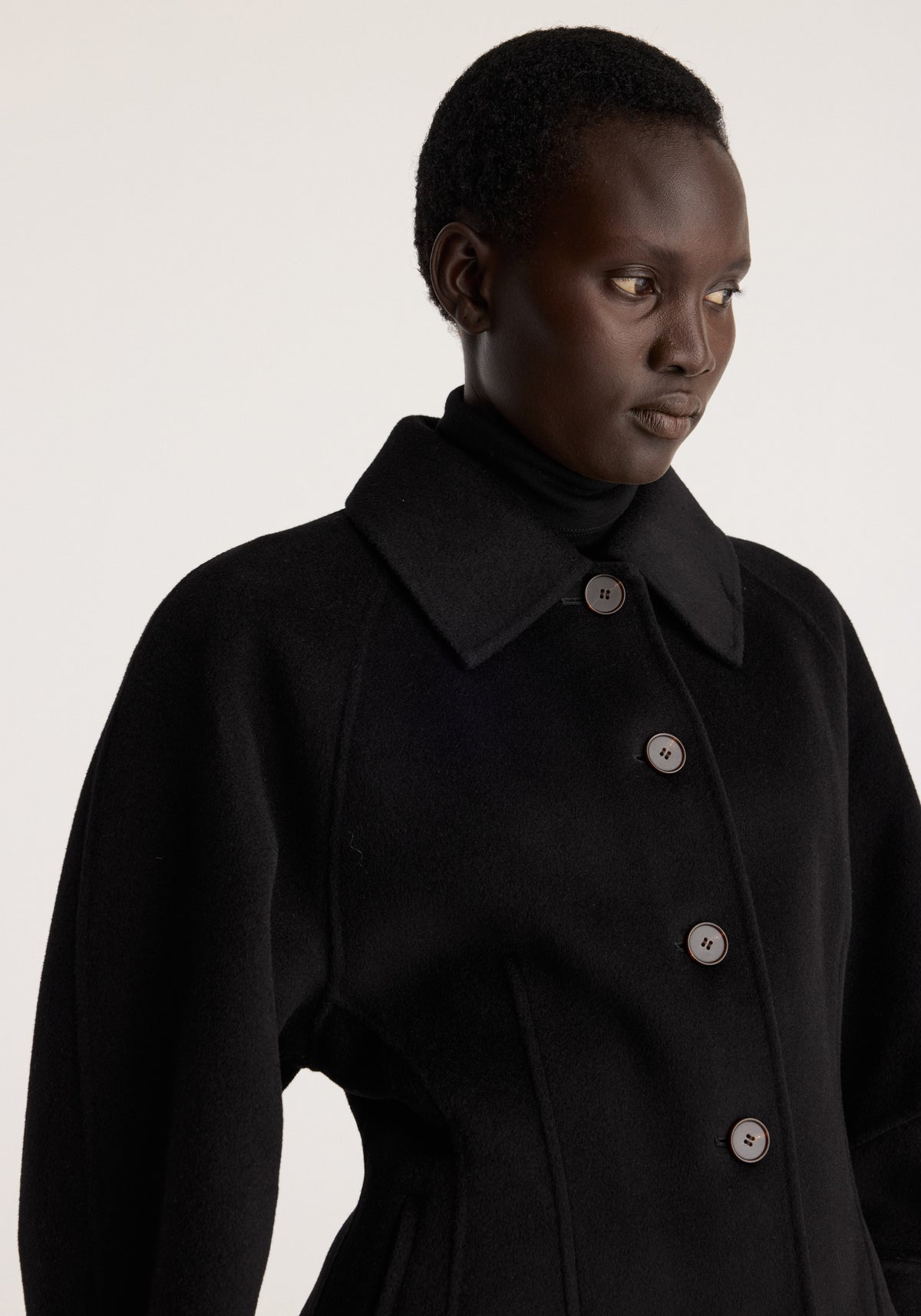 Double-faced sculptural jacket | black worn by a model featuring an oversized collar sculpted waist and four visible front buttons