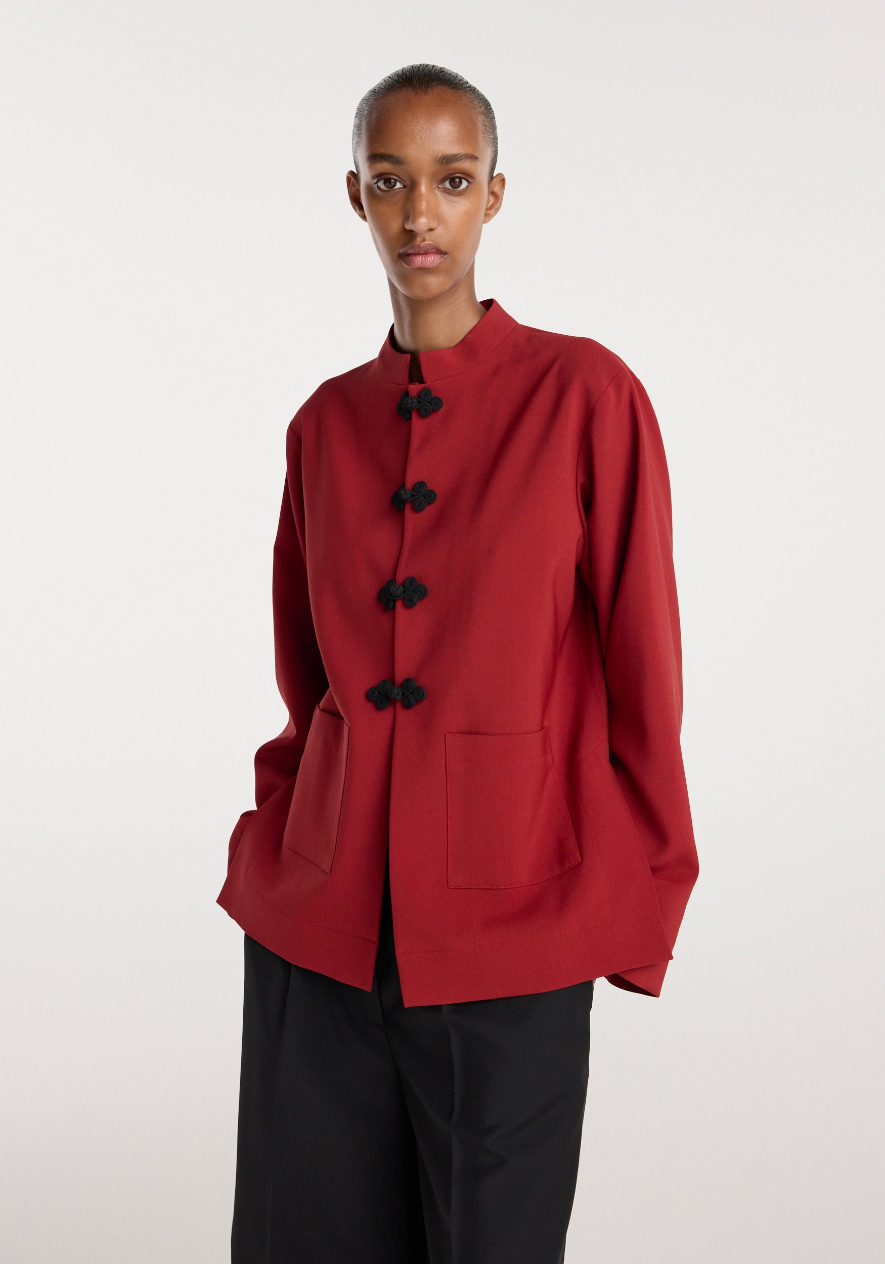 Model wearing a carmine Pankou closure jacket featuring traditional knotted buttons, front patch pockets, and a stand collar, paired with black trousers.