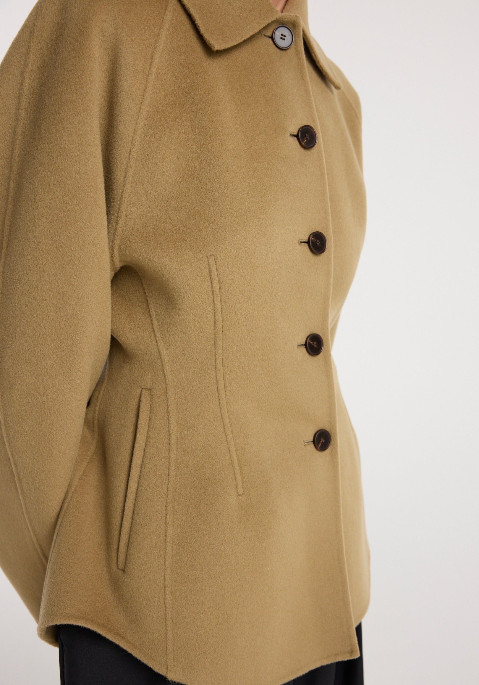 Close-up of a camel-colored Double-faced sculptural jacket | camel with a structured collar, button front closure, and slanted side pockets, showcasing its tailored fit and smooth fabric texture.