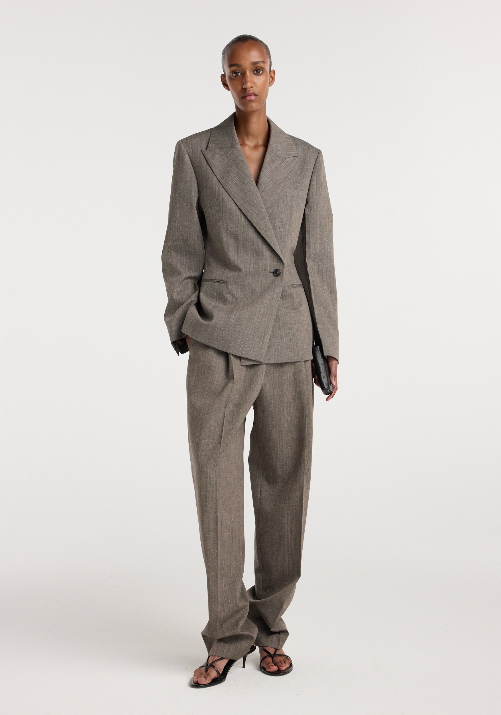 Model wearing a tailored hourglass shaped blazer | earth slub in a muted earth tone, paired with matching wide-leg trousers and black open-toe heels, standing against a plain white background.