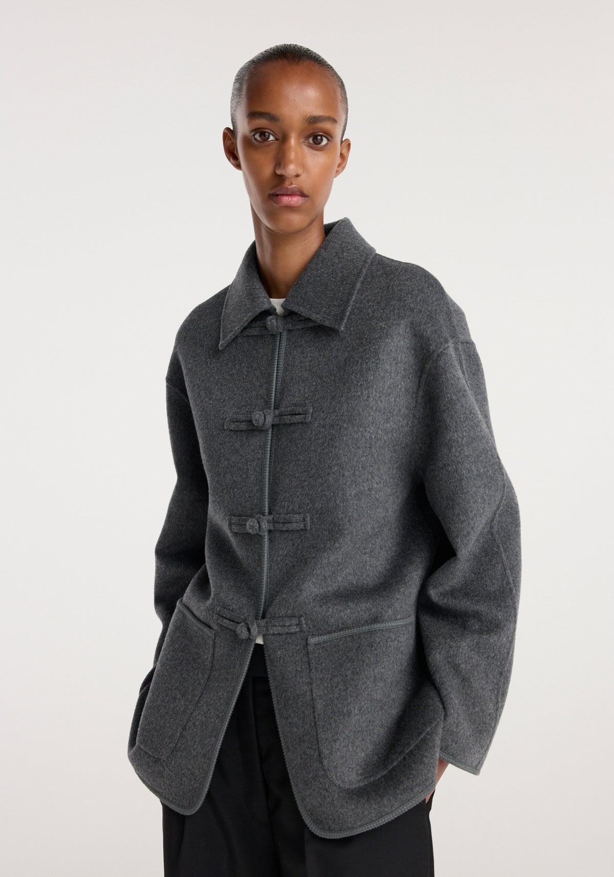 Model wearing a dark grey melange double-faced wool pankou closure jacket | dark grey melange with large patch pockets and a classic collar against a plain light background.