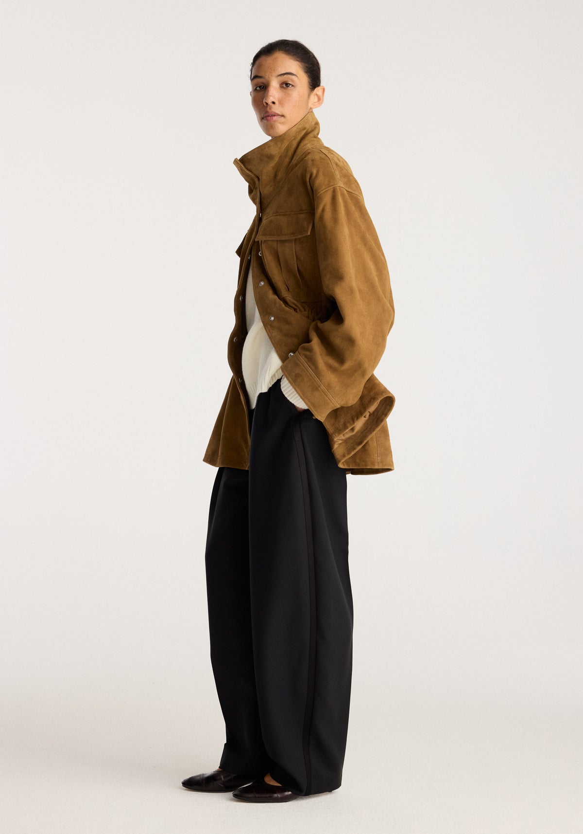 Sculptural suede jacket | sage shown on a model in profile with a structured silhouette, front pockets, long sleeves, and a high collar over black trousers