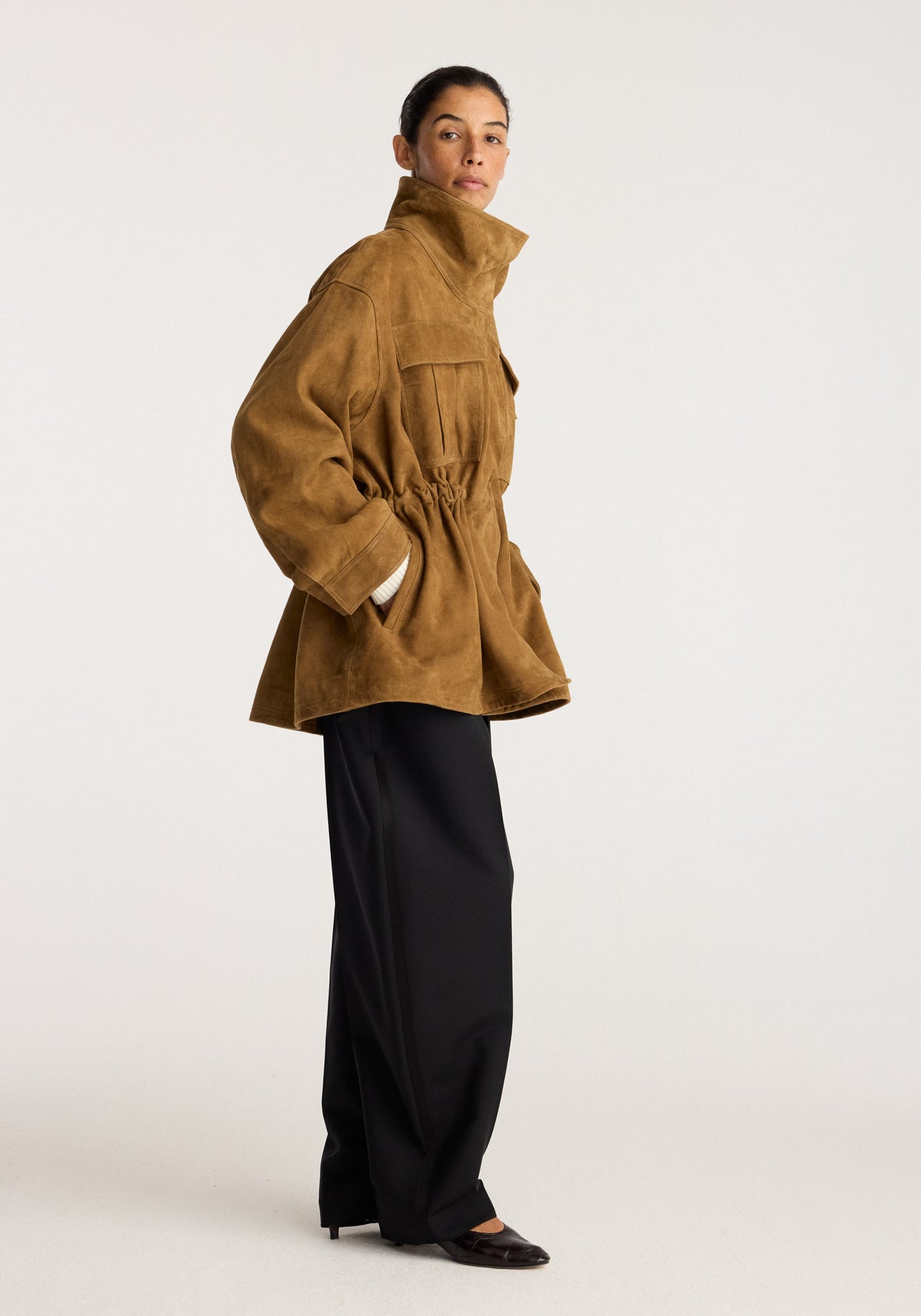 Sculptural suede jacket | sage worn by a model with a high collar and cinched waist styled with wide black trousers and loafers