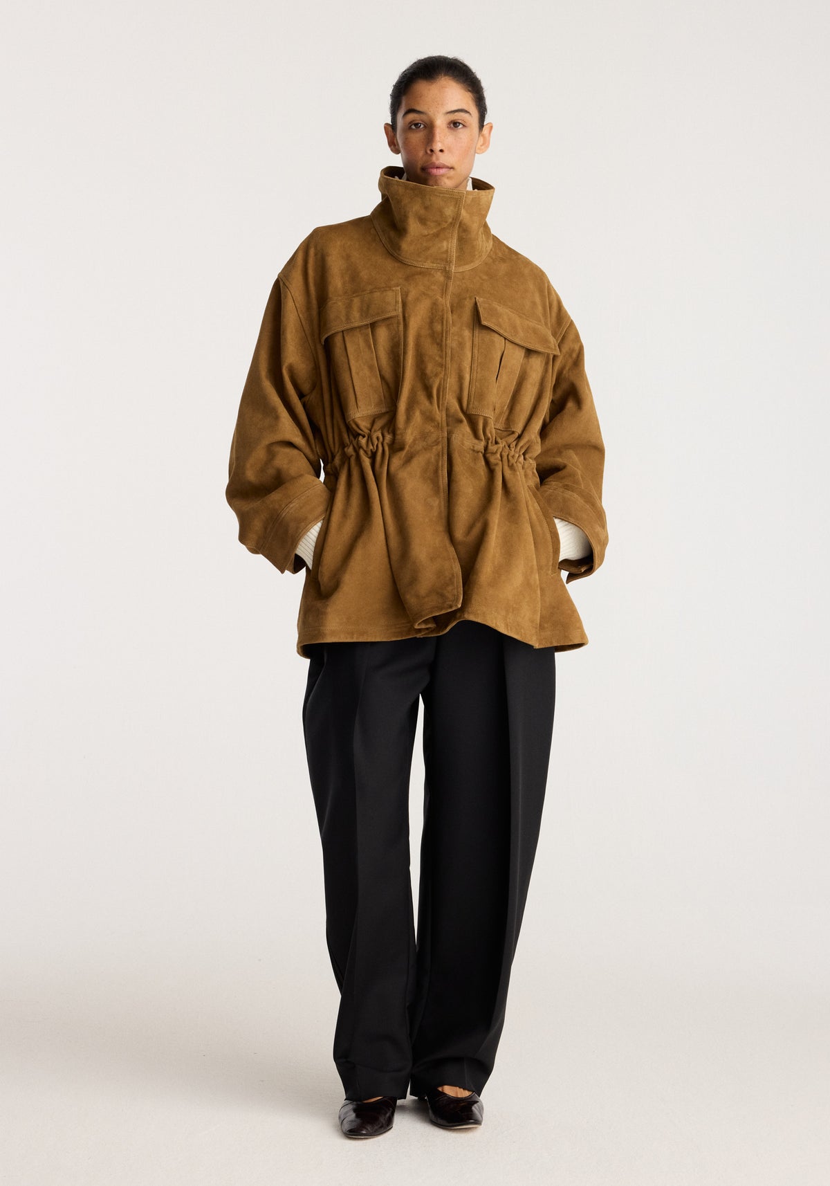 Sculptural suede jacket | sage shown on a model with a high collar front pockets gathered waist and relaxed sleeves over black trousers