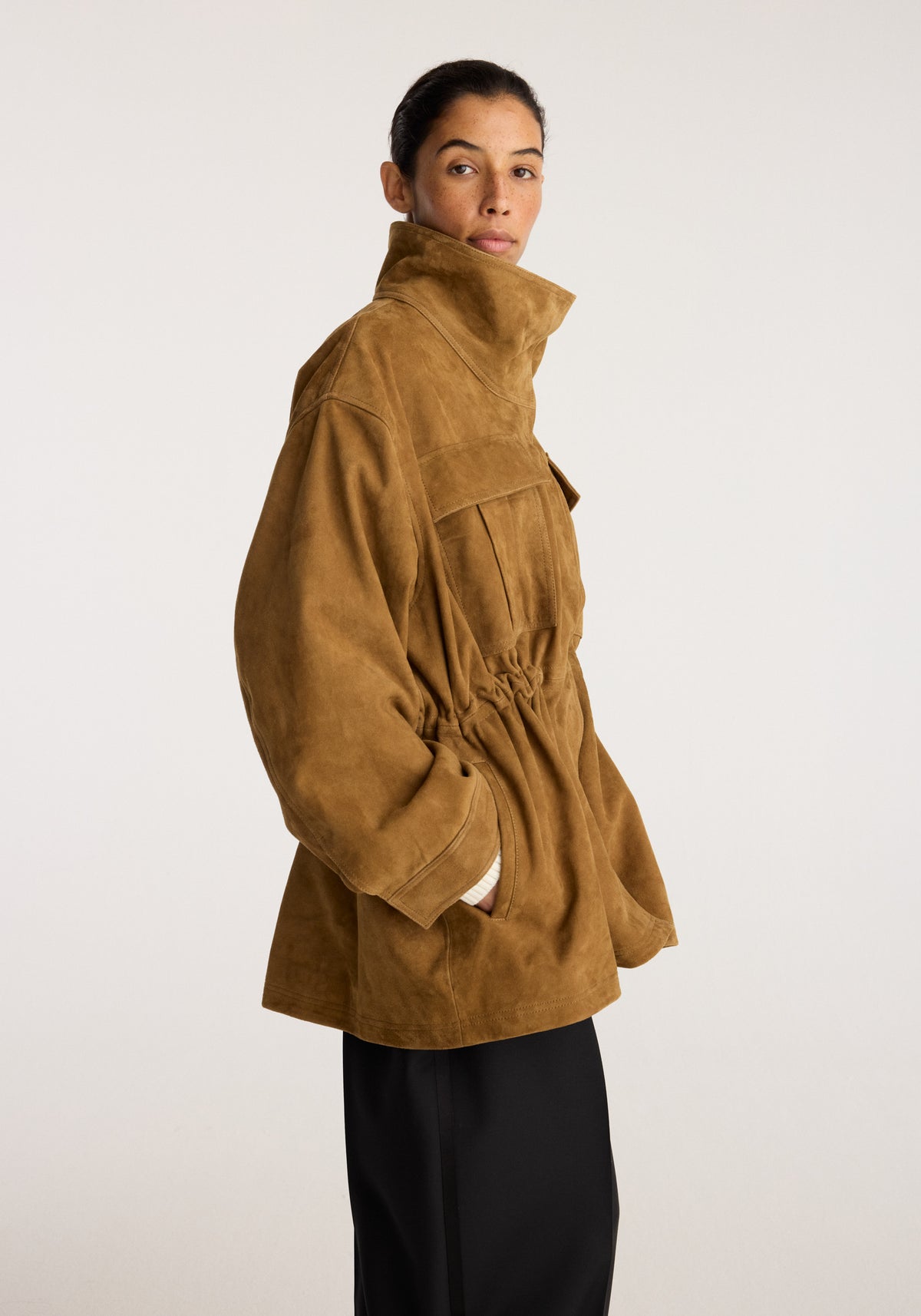 Sculptural suede jacket | sage shown on a model in side profile with a high collar gathered waist long sleeves and utility pockets