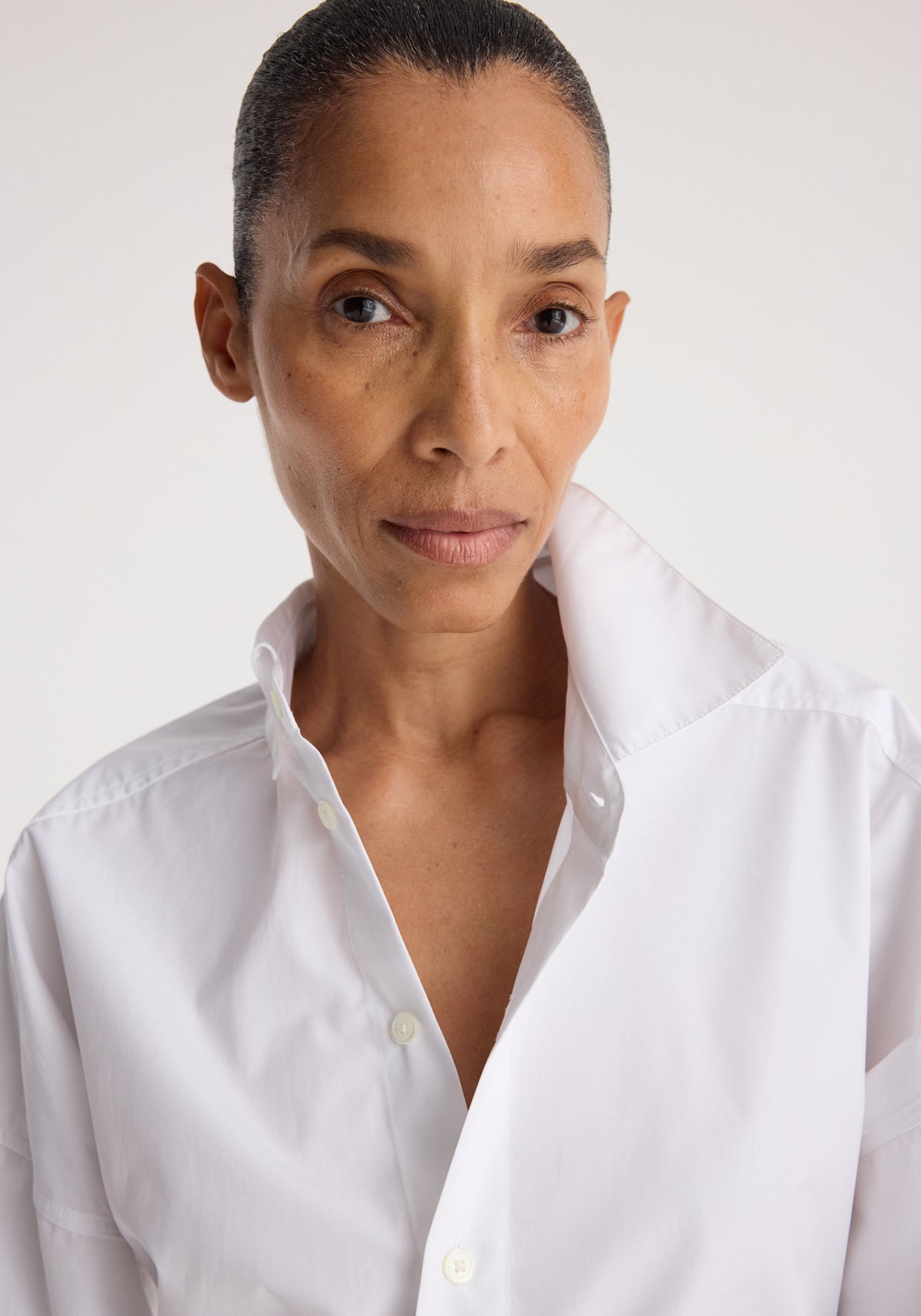 Close-up of a woman wearing a Poplin uneven collar shirt | optic white with the collar stylishly turned up, showcasing the shirt’s crisp and clean design.