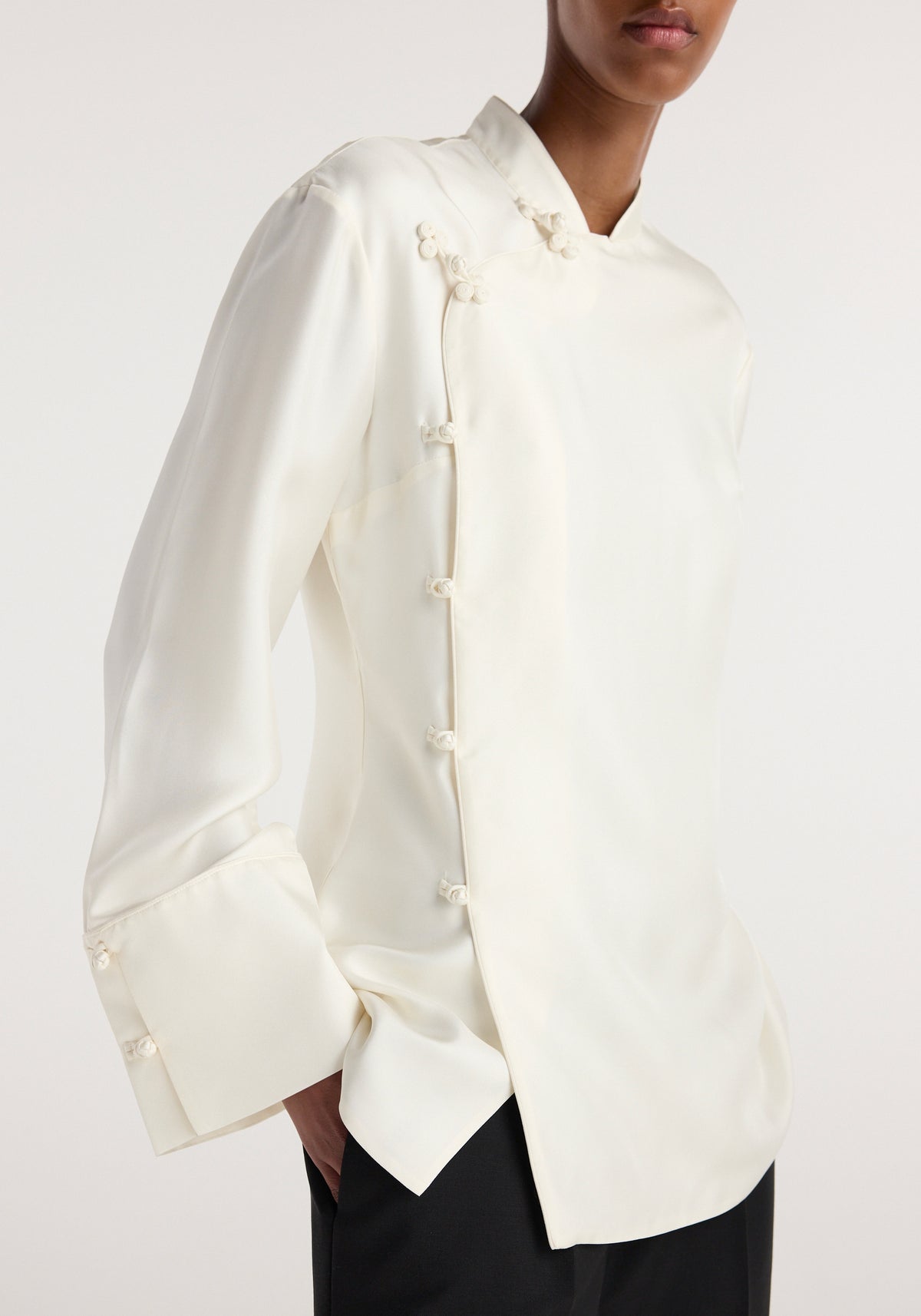 Model wearing a cream silk top with a pankou closure featuring decorative Chinese knot buttons on the front and cuffs, styled with black pants, Pankou closure silk top | cream.