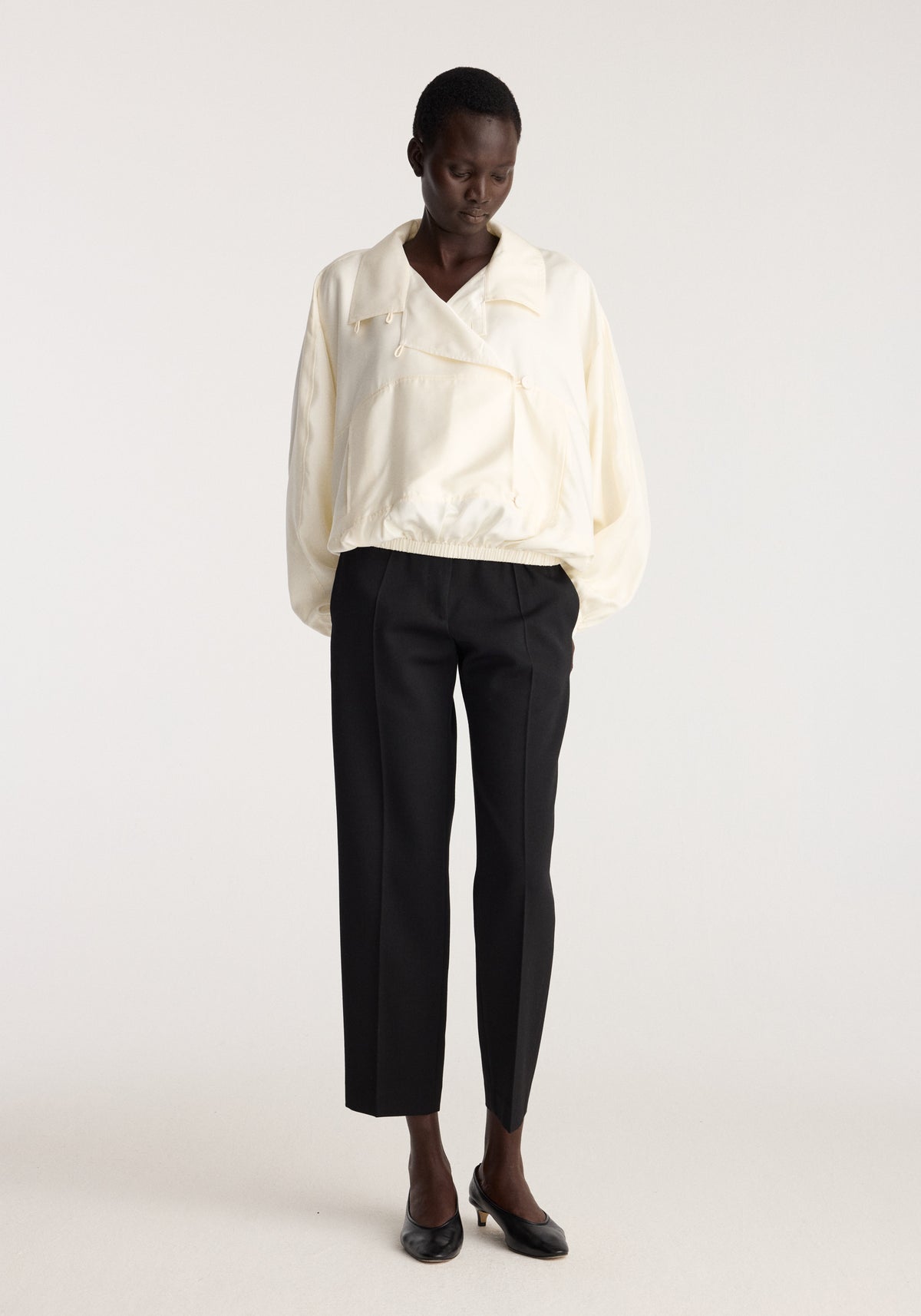Silk blouson anorak | cream worn with black trousers and loafers by a model in a minimalist studio setting