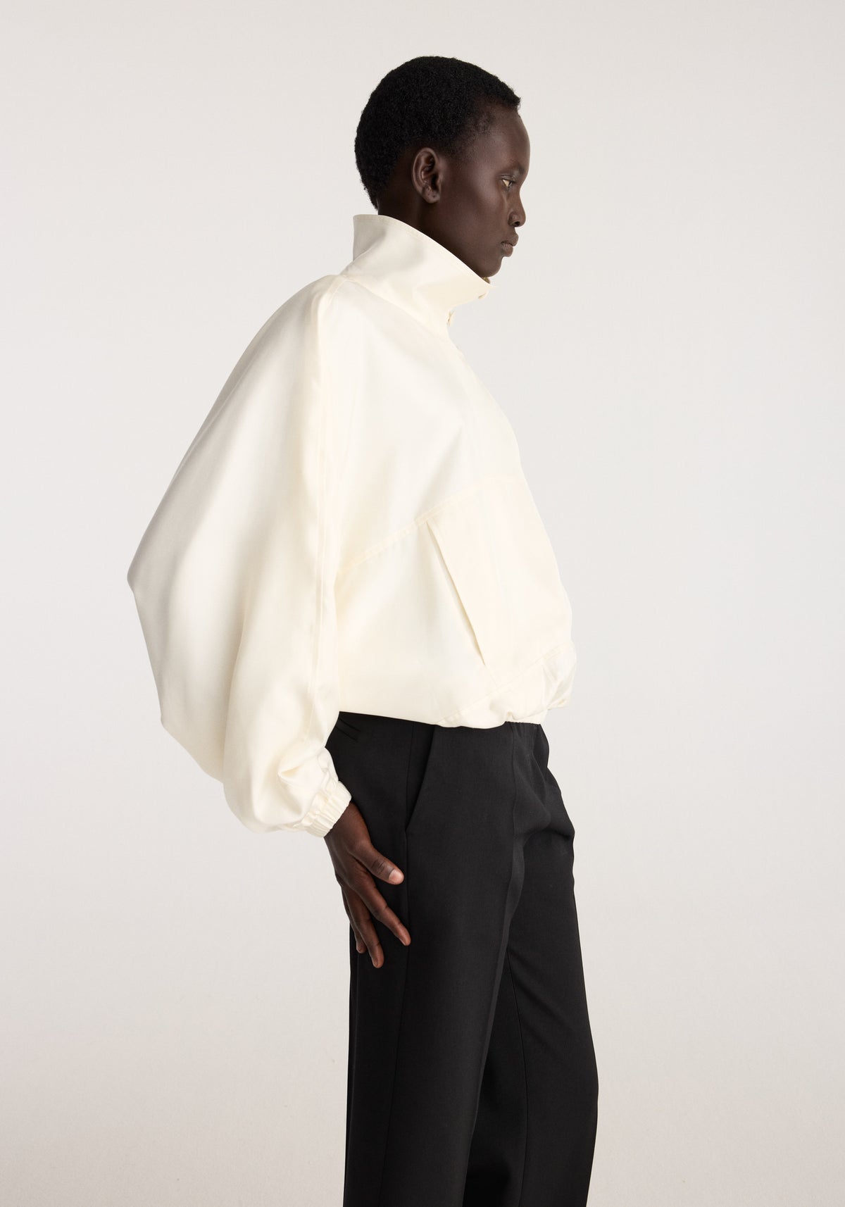 Silk blouson anorak | cream shown on a model in profile with a high collar elastic cuffs and relaxed silhouette paired with black trousers