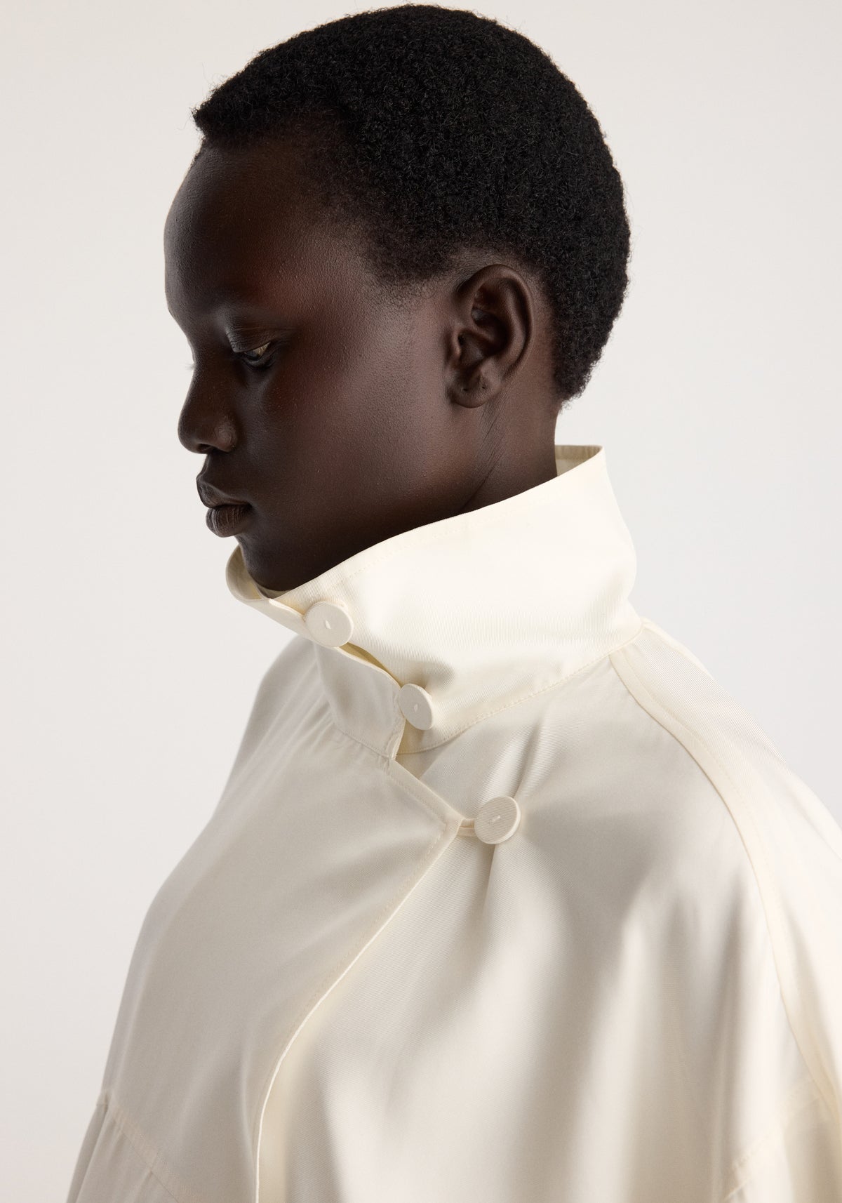 Silk blouson anorak | cream shown on a model in side profile with a high collar and button fastening in soft cream silk