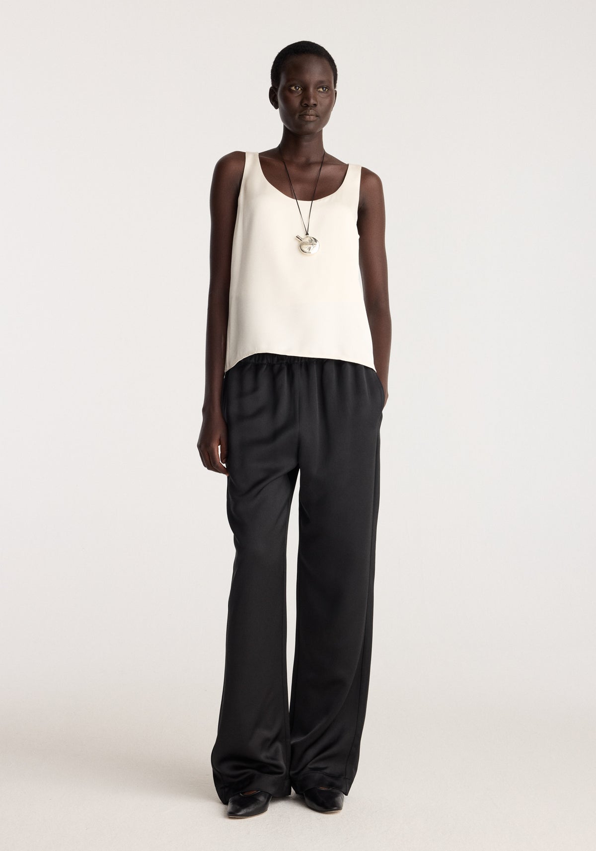 Satin scoop-neck top | ivory worn by a model with black wide-leg trousers and layered necklaces in a minimalist studio setting