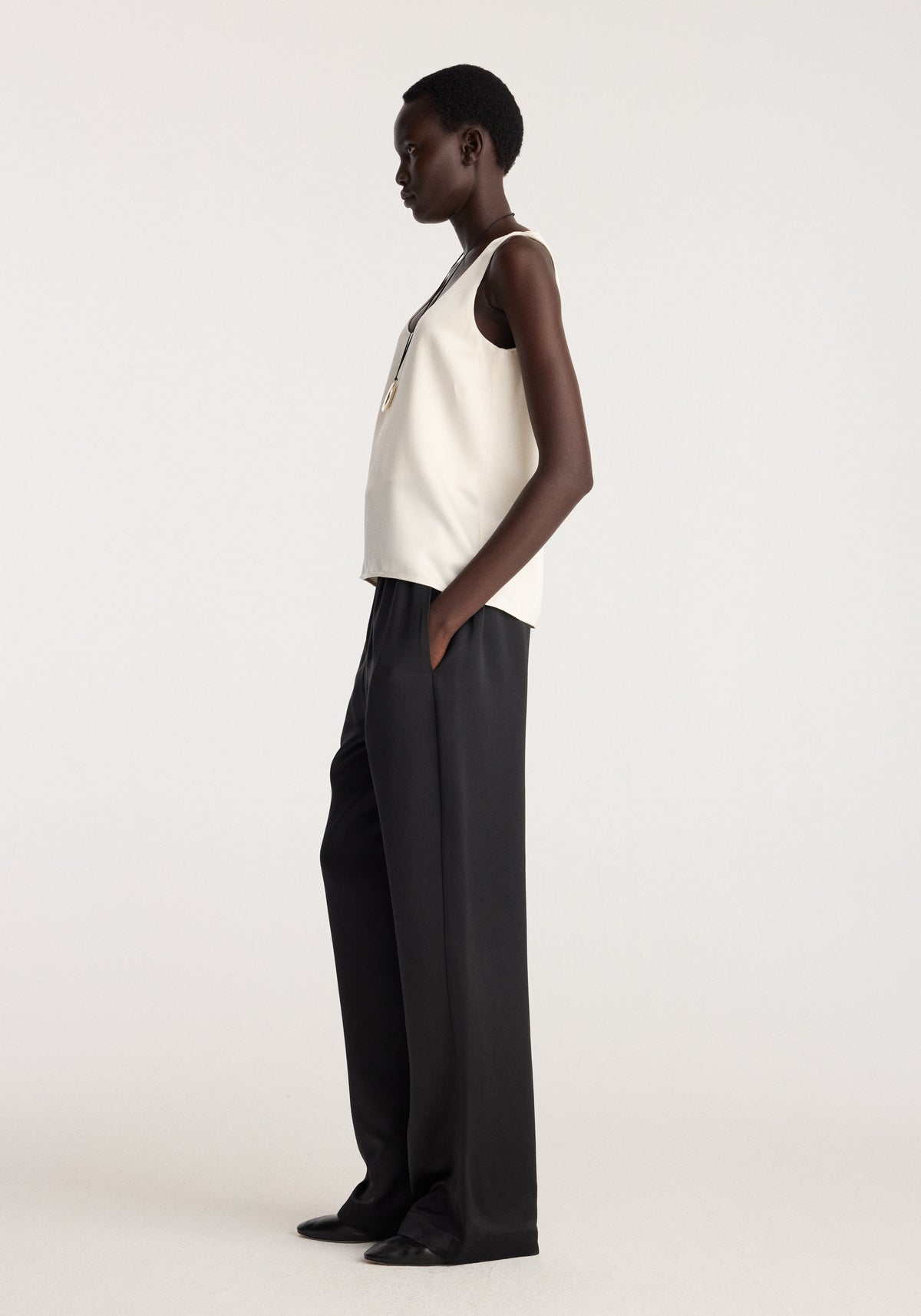Model wearing Satin scoop-neck top | ivory with black trousers, shown in side profile against a neutral studio background
