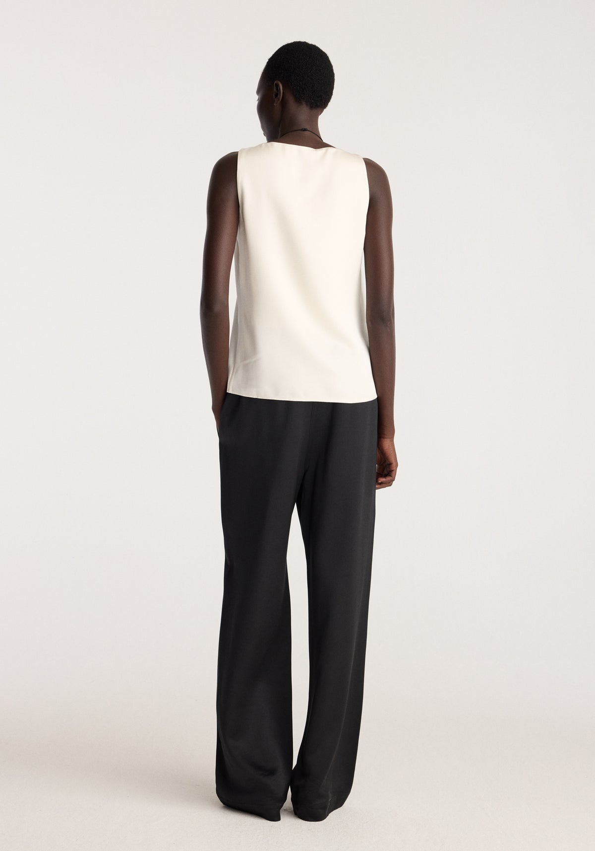 Satin scoop-neck top | ivory shown from the back on a model, featuring a sleeveless cut and smooth ivory fabric styled with black trousers
