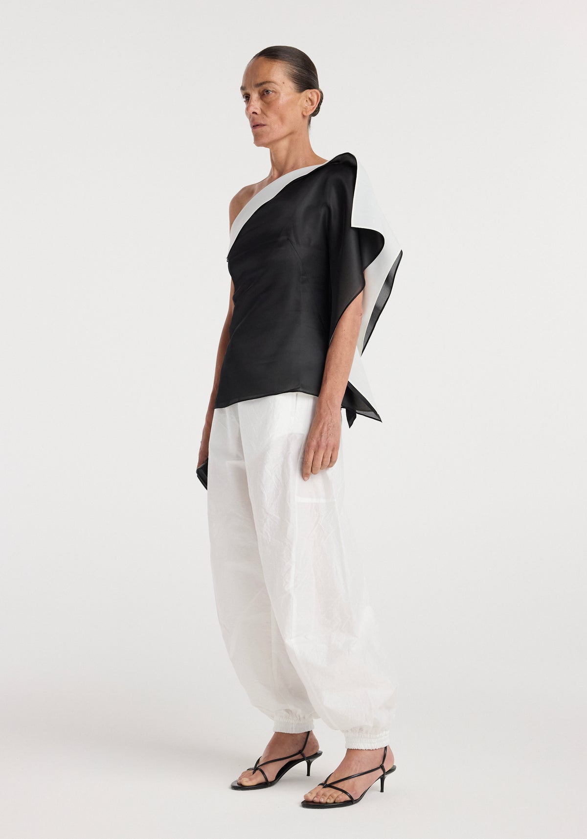 Woman wearing a black and white sculptural double layered top | black with an asymmetrical design, paired with loose white pants and black strappy heels.