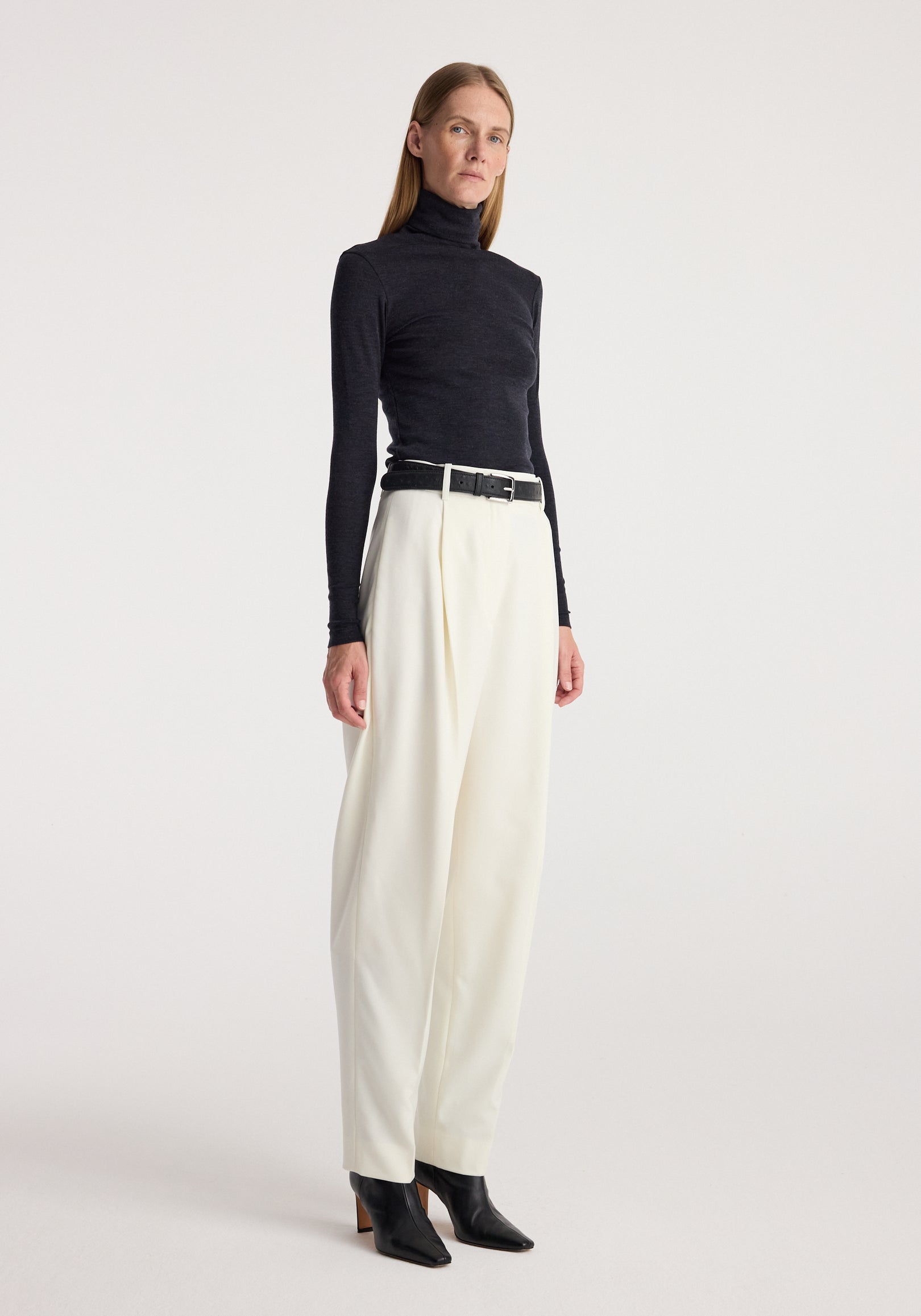 Woman wearing a charcoal fitted long-sleeve Fine merino turtleneck | anthracite melange paired with high-waisted white wide-leg pants and black ankle boots.