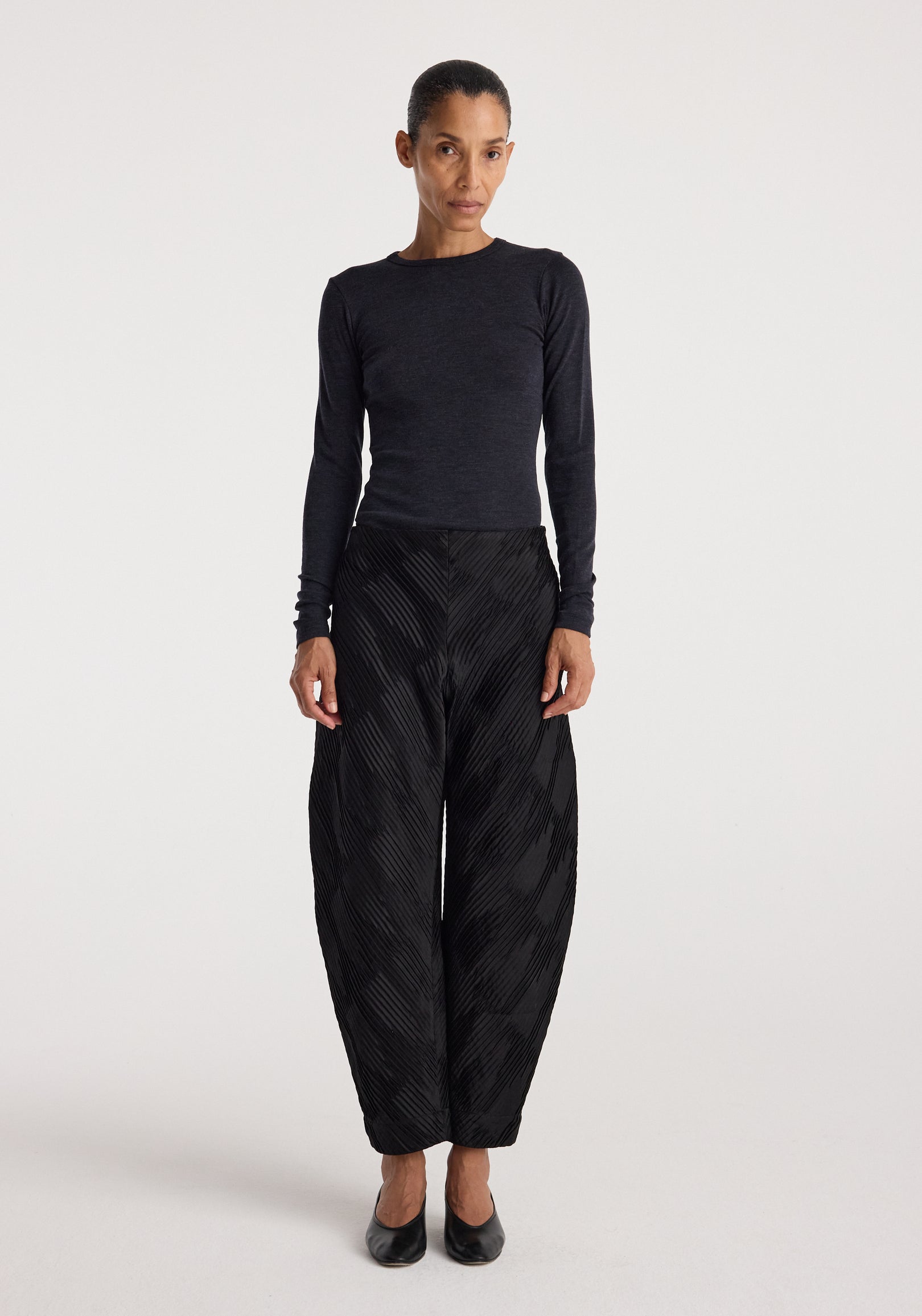 Woman wearing a fine merino long sleeve | anthracite melange top paired with black textured wide-leg pants and black shoes, standing against a plain white background.