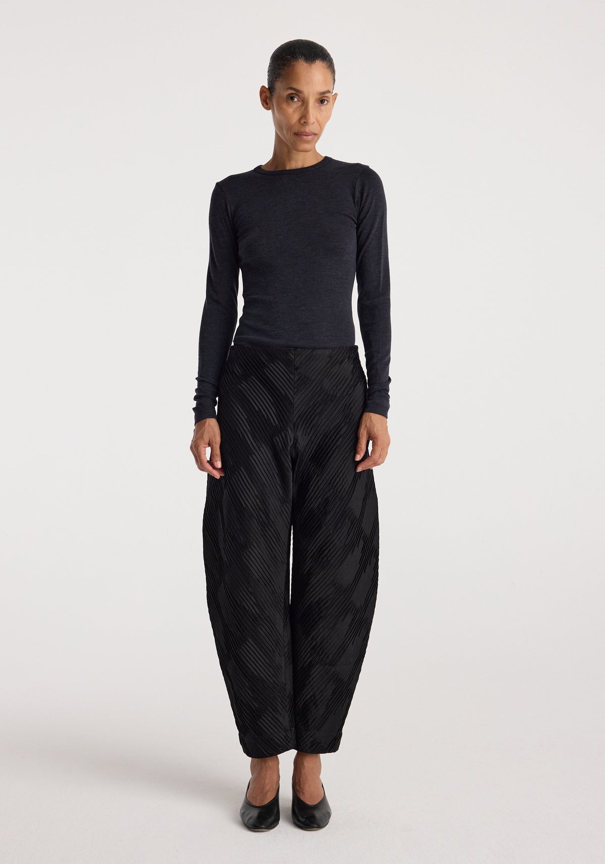 Woman wearing a fine merino long sleeve | anthracite melange top paired with black textured wide-leg pants and black shoes, standing against a plain white background.