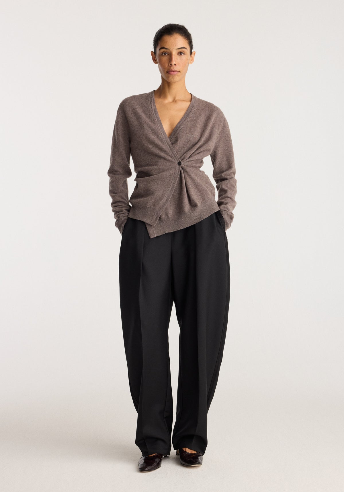 Twisted ballet cardigan | mud worn by a model with black wide leg trousers and black shoes in a studio setting