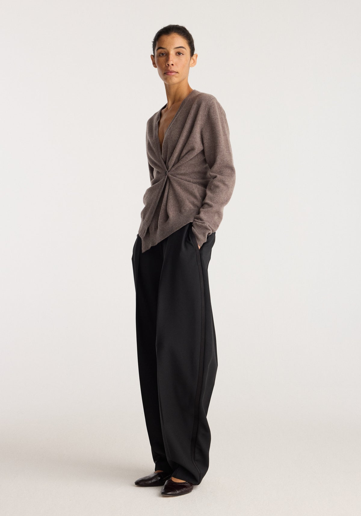Twisted ballet cardigan | mud worn by a model with a twisted front and long sleeves styled with black wide leg trousers and dark shoes