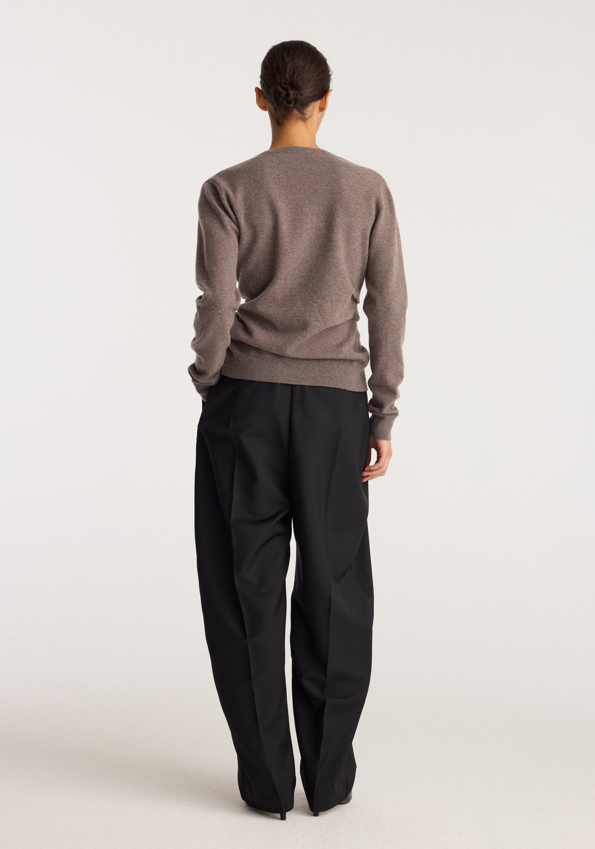 Twisted ballet cardigan | mud shown from the back on a model wearing a brown cardigan with long sleeves and black trousers in a studio setting