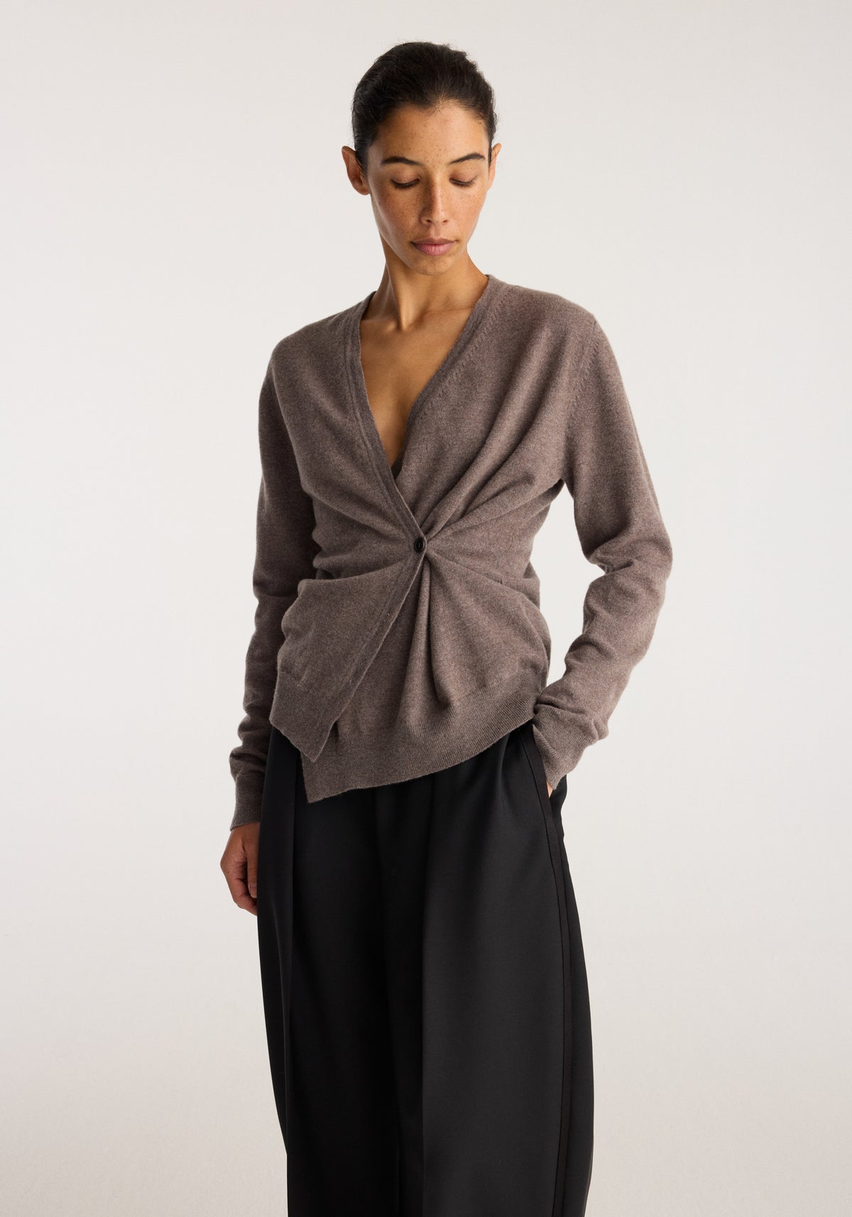 Twisted ballet cardigan | mud in a soft brown knit with a twisted front detail worn with flowing black trousers by a model posing against a neutral backdrop