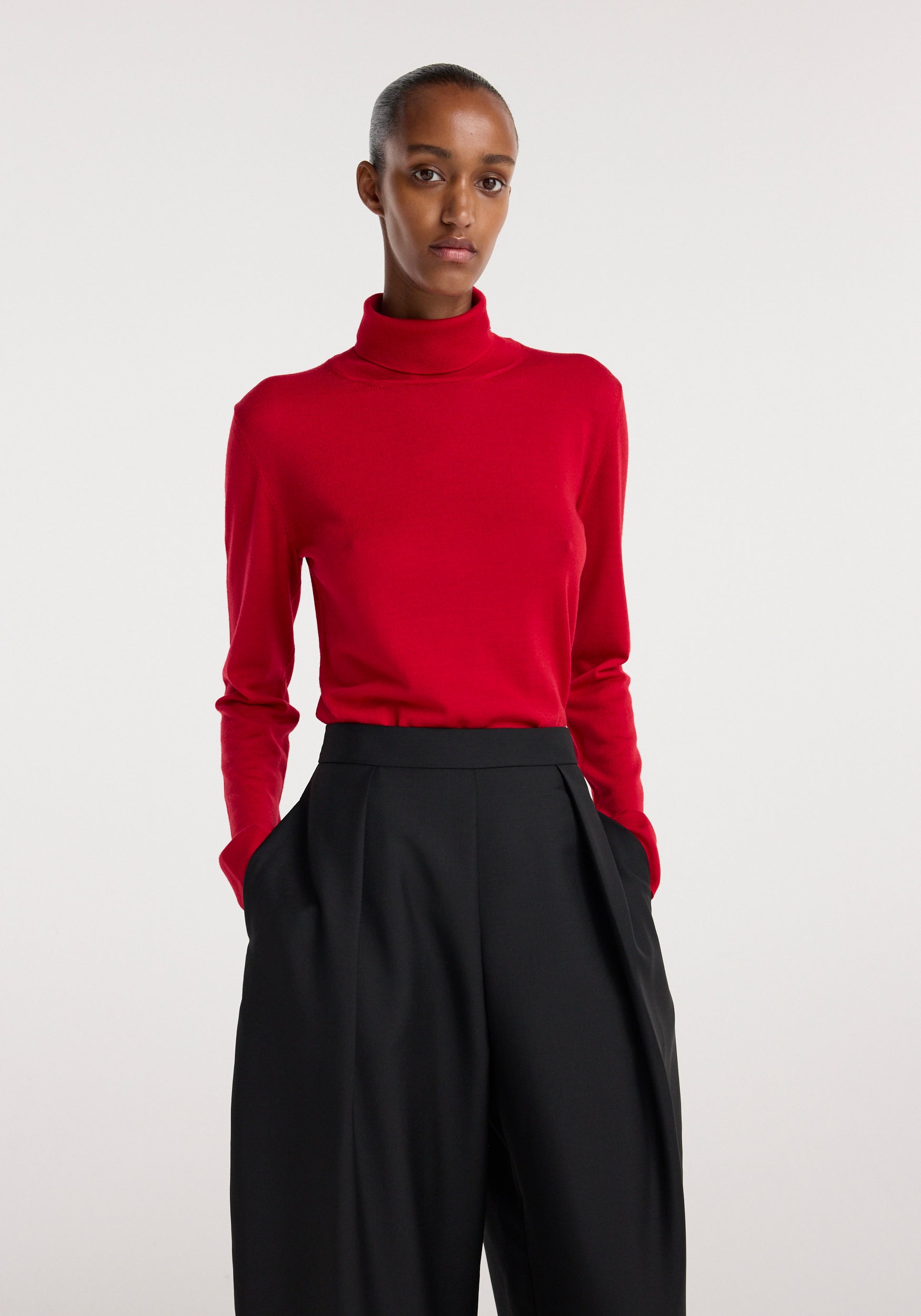 Woman wearing a red fine-knit wool cashmere turtleneck paired with high-waisted black wide-leg pants against a plain background.