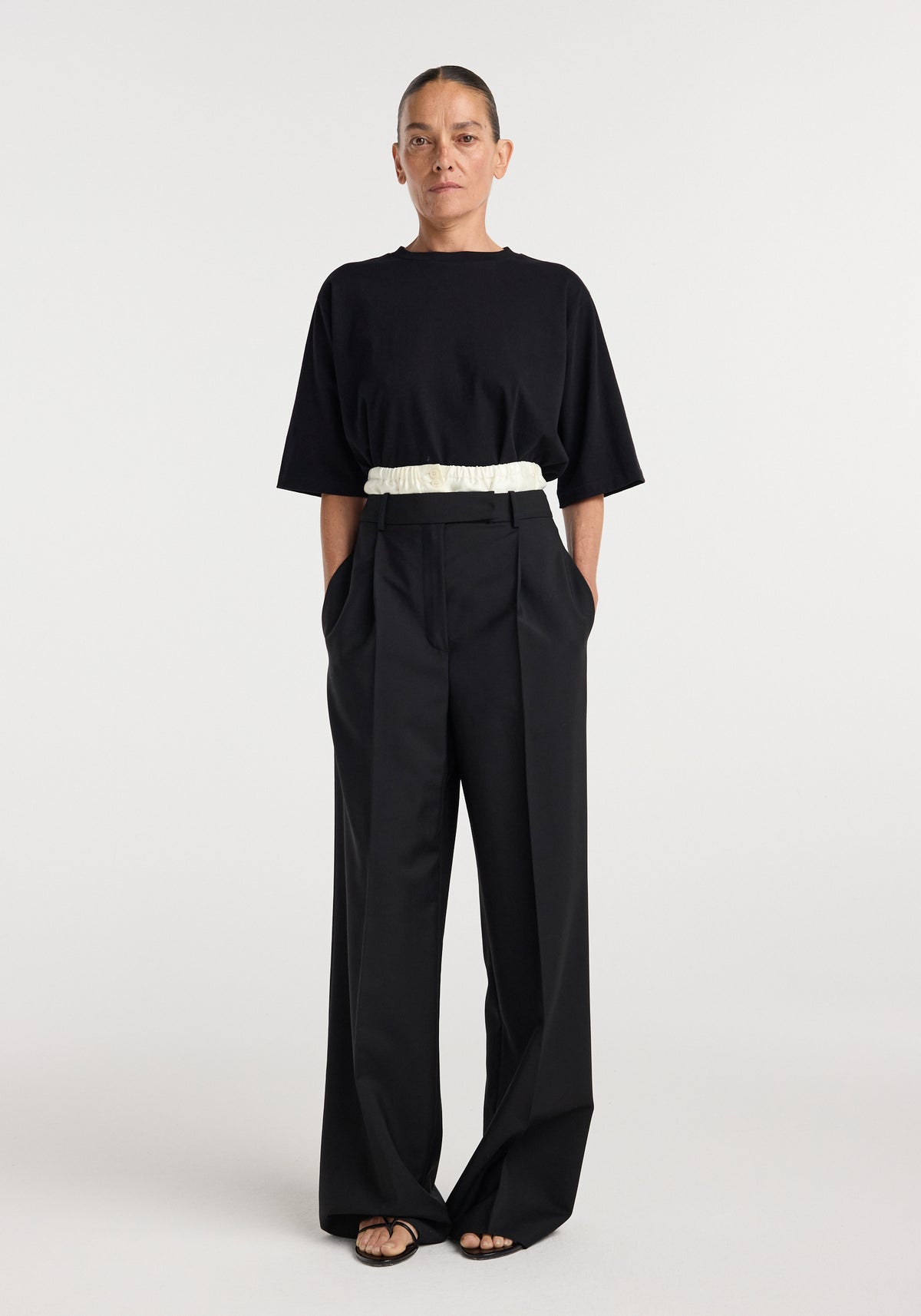 Woman wearing black loose-fitting Boxer detailed trousers | black with wide legs, front pleats, side pockets, and a high waist paired with a black oversized top and sandals.