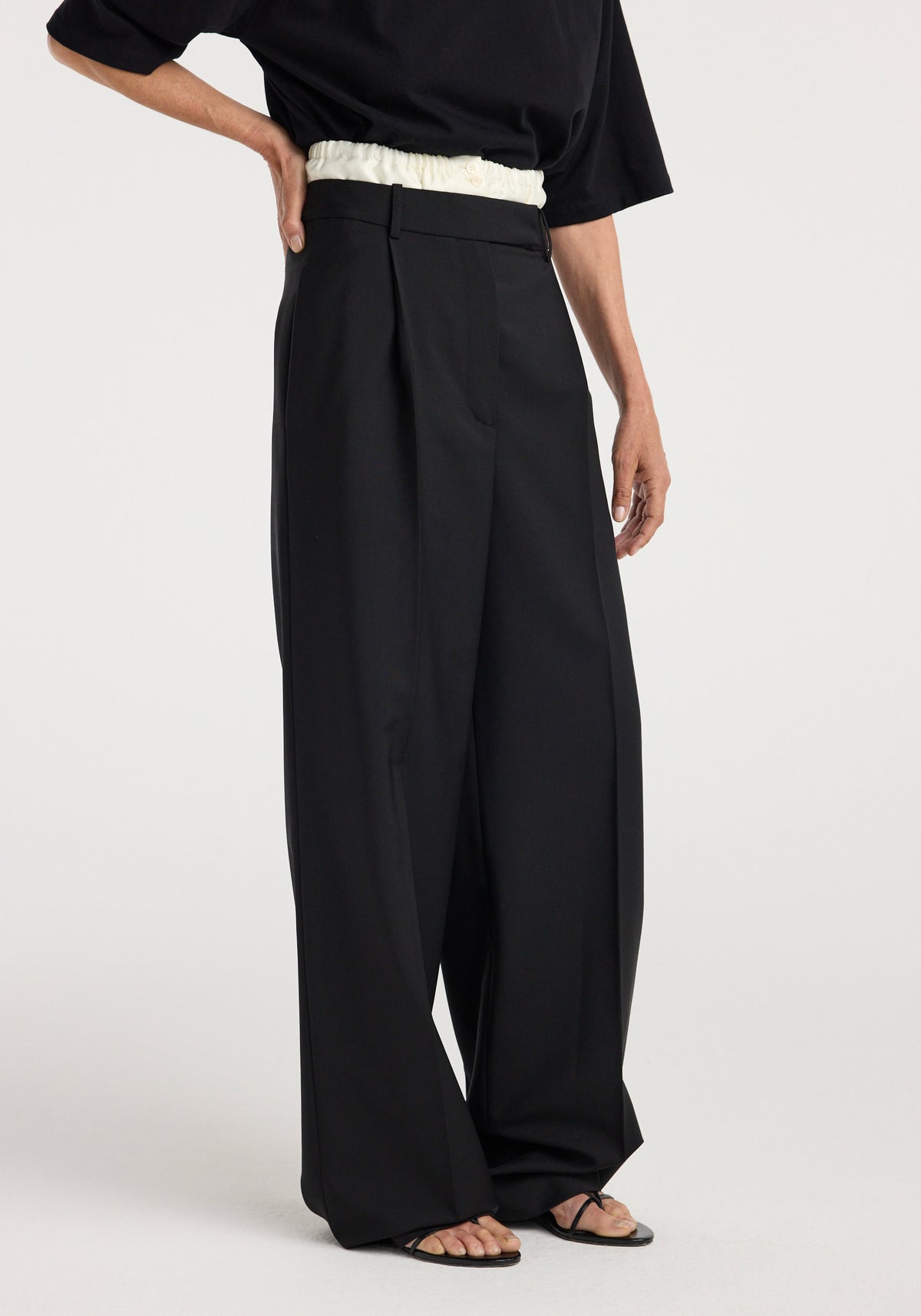 Model wearing loose-fitting black Boxer detailed trousers | black with a high waist and wide legs paired with a black top and sandals against a light background.