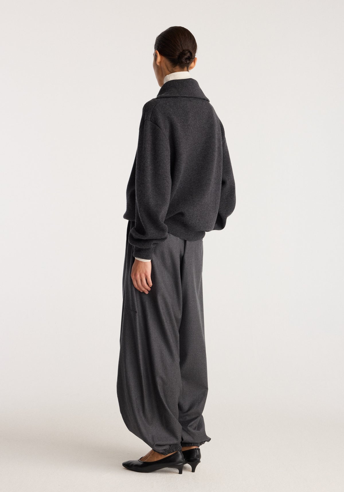 Back view of a model wearing Balloon track pants | dark grey melange with a relaxed balloon silhouette and tapered ankles styled with black shoes