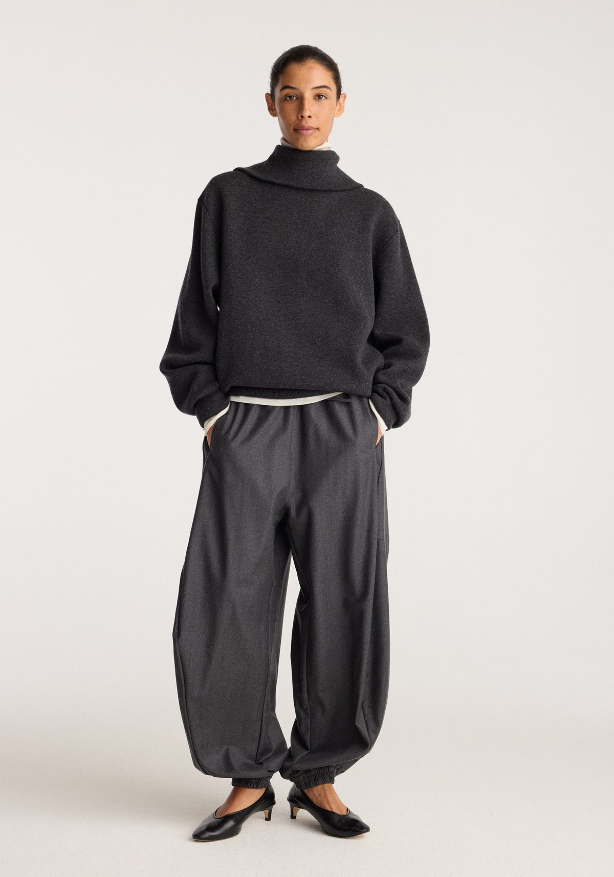 Balloon track pants | dark grey melange worn with a dark oversized sweater and black flats on a model against a neutral studio background