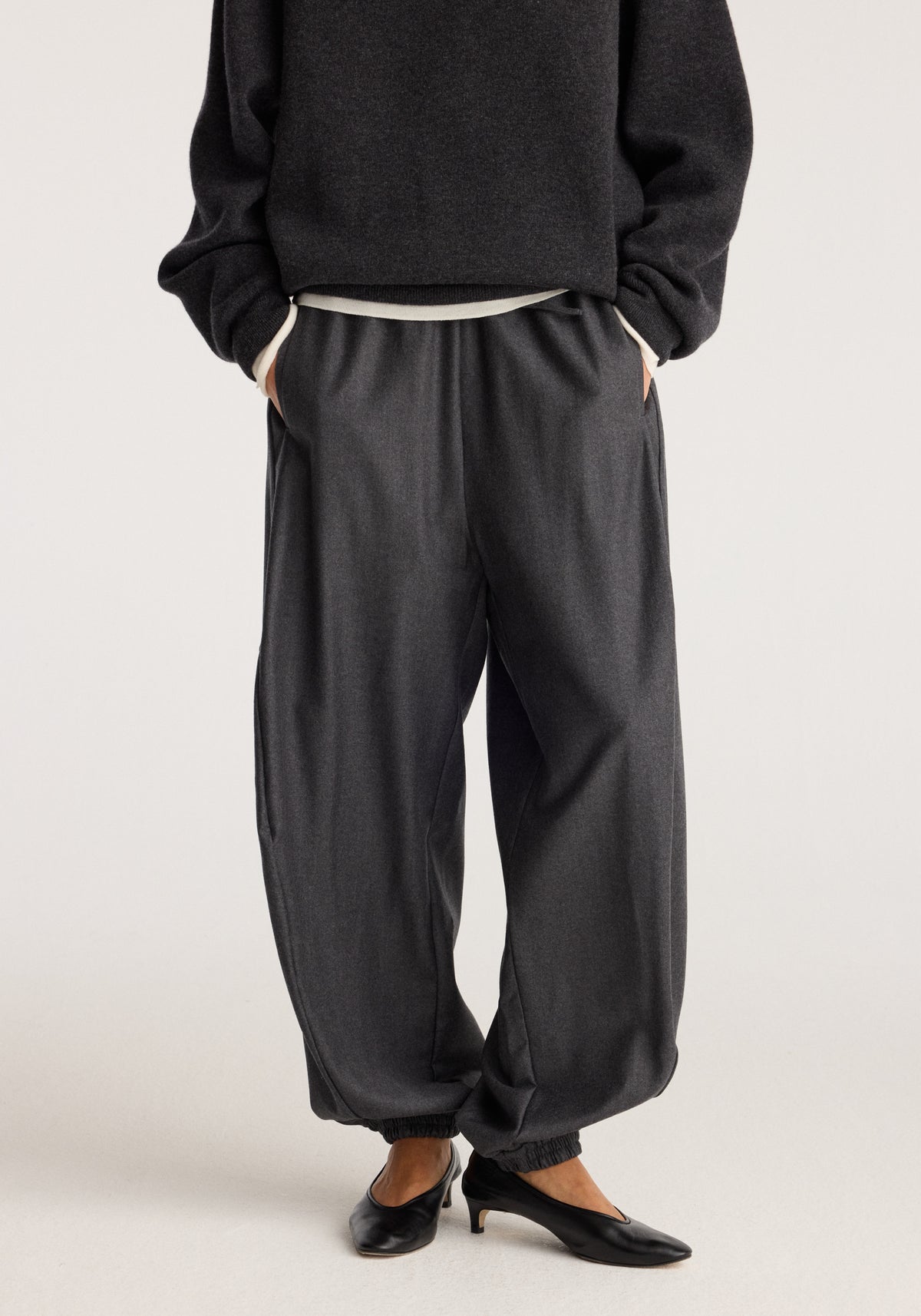 Balloon track pants | dark grey melange shown on a model with a relaxed balloon fit, elastic cuffs, side pockets and black ballet flats