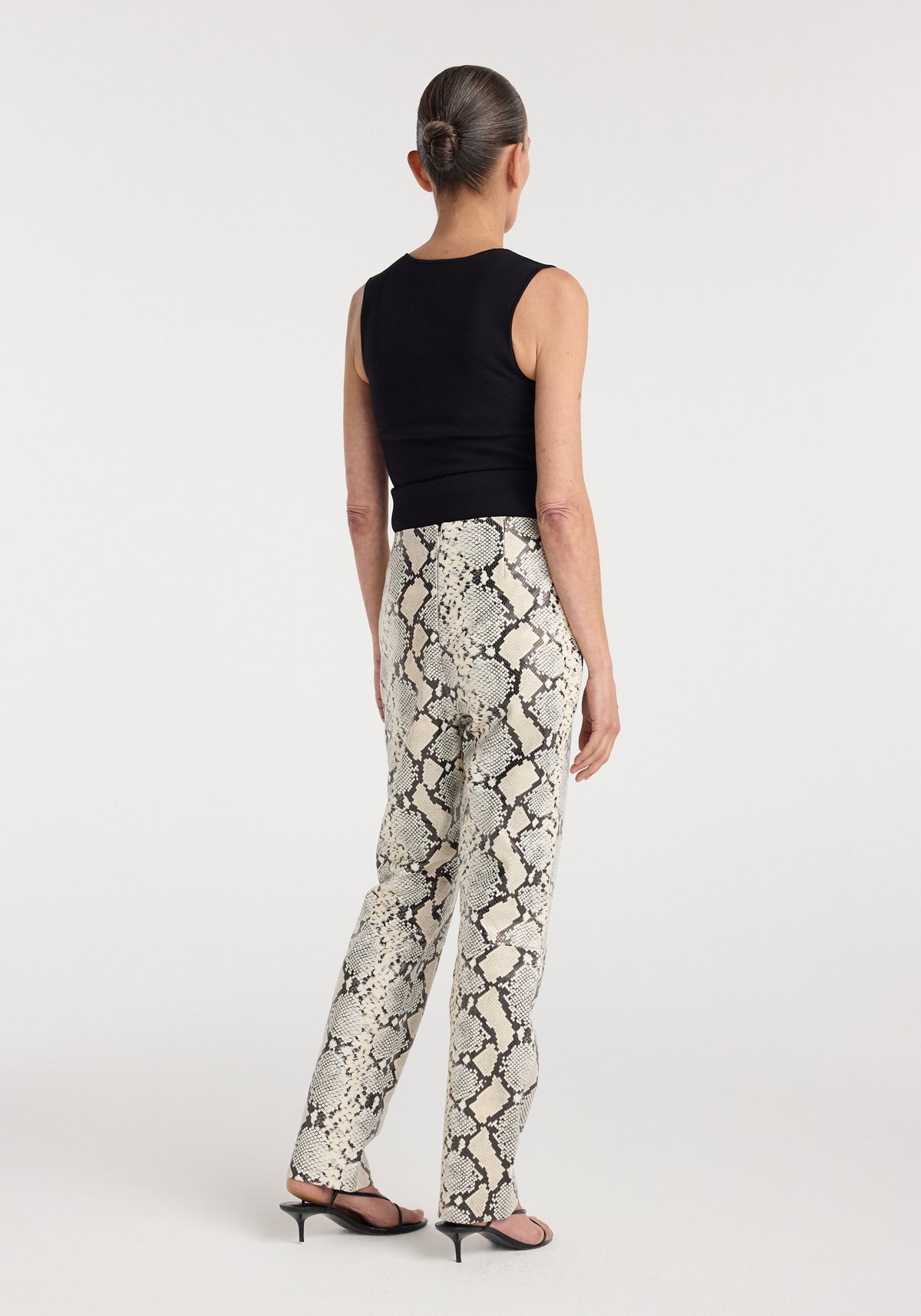 Snakeskin leather trousers | snakeskin shown from the back on a model wearing a black sleeveless top and heels, featuring a neutral snakeskin pattern and wide leg fit