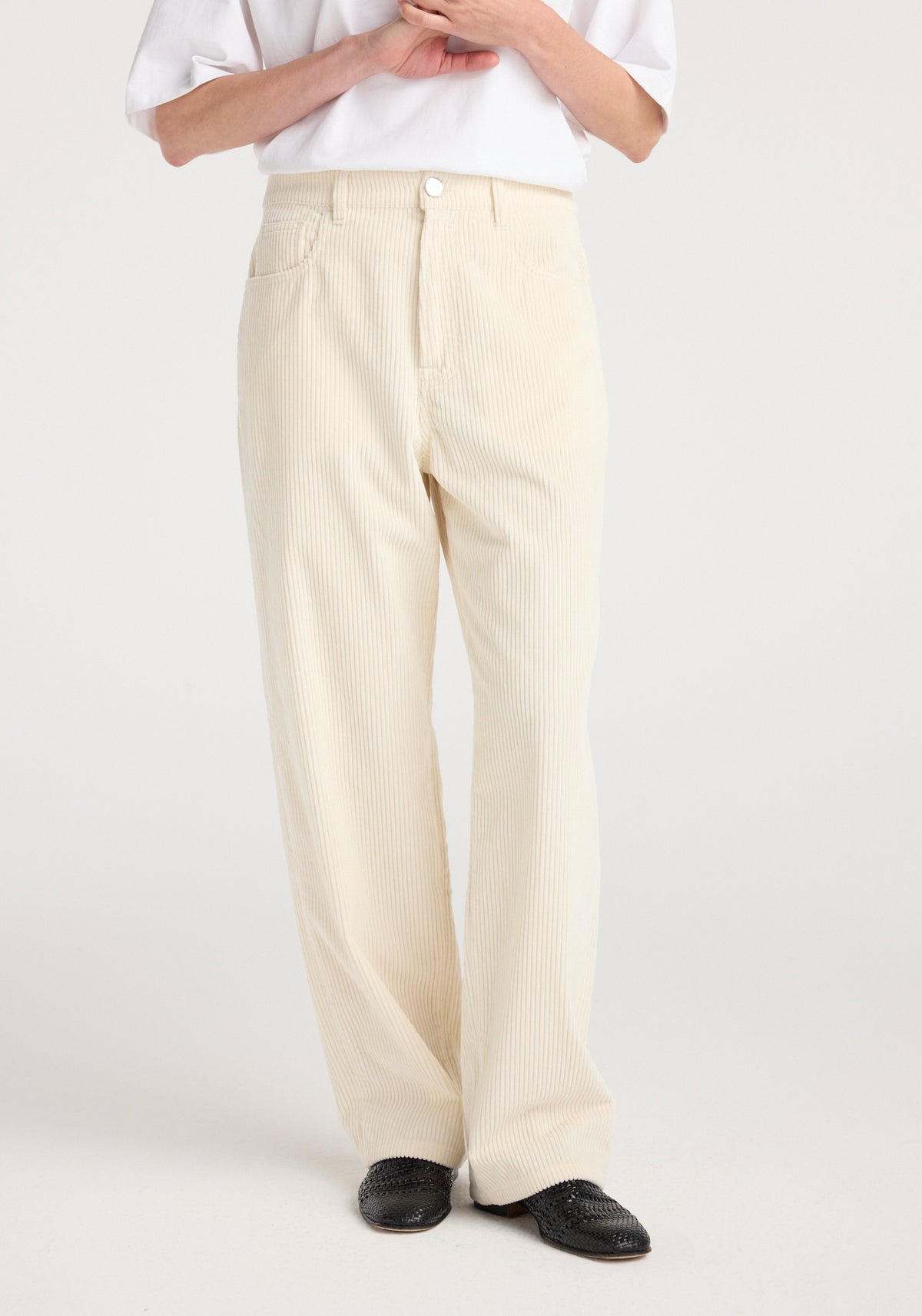 Front view of a person wearing Bruun - Signature baggy corduroy | winter white pants with a relaxed fit, paired with black woven shoes and a white top.