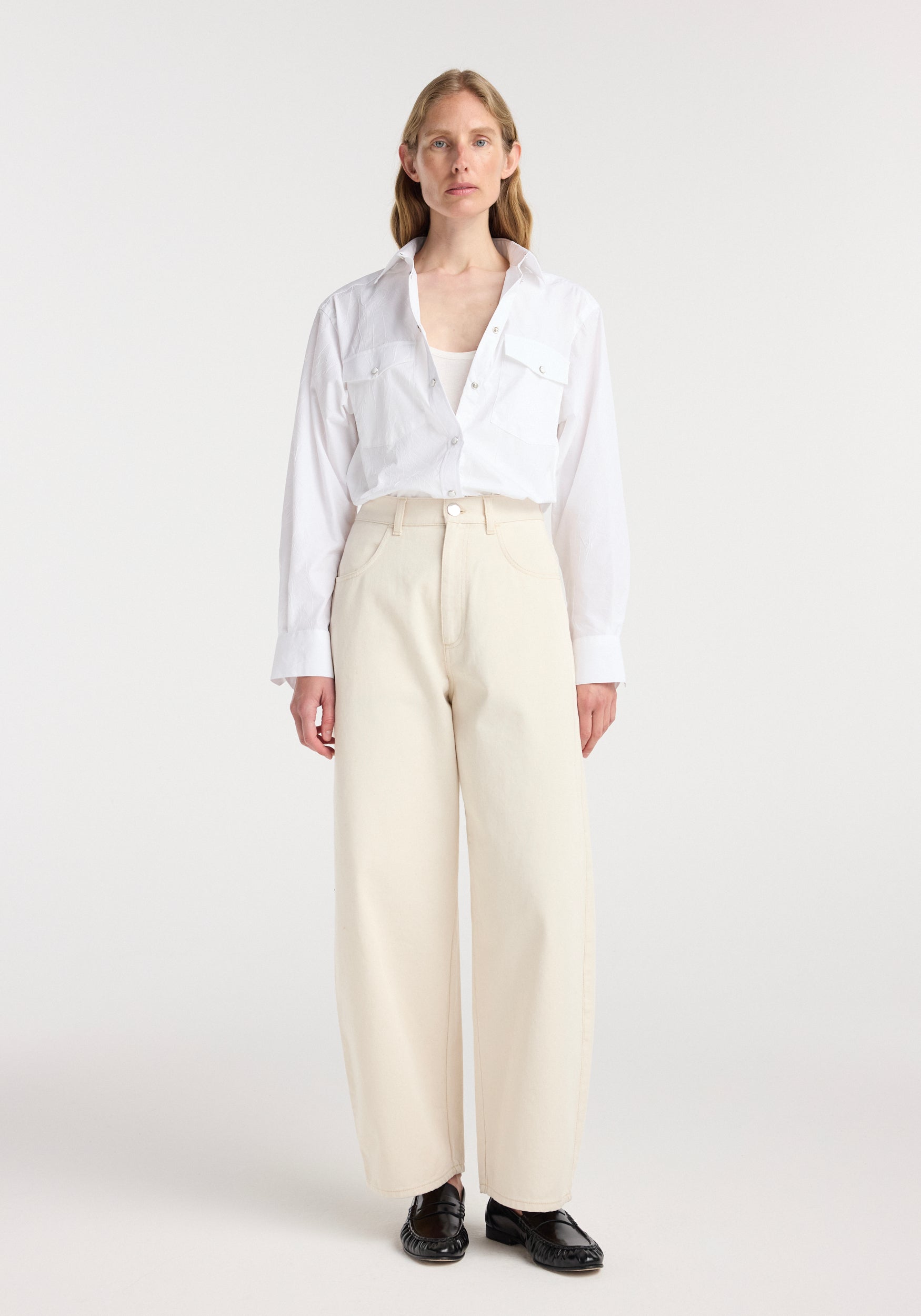 Woman wearing a white button-up shirt and ecru wide-leg pants standing against a plain background, showcasing the Berber - Barrel leg denim | ecru.