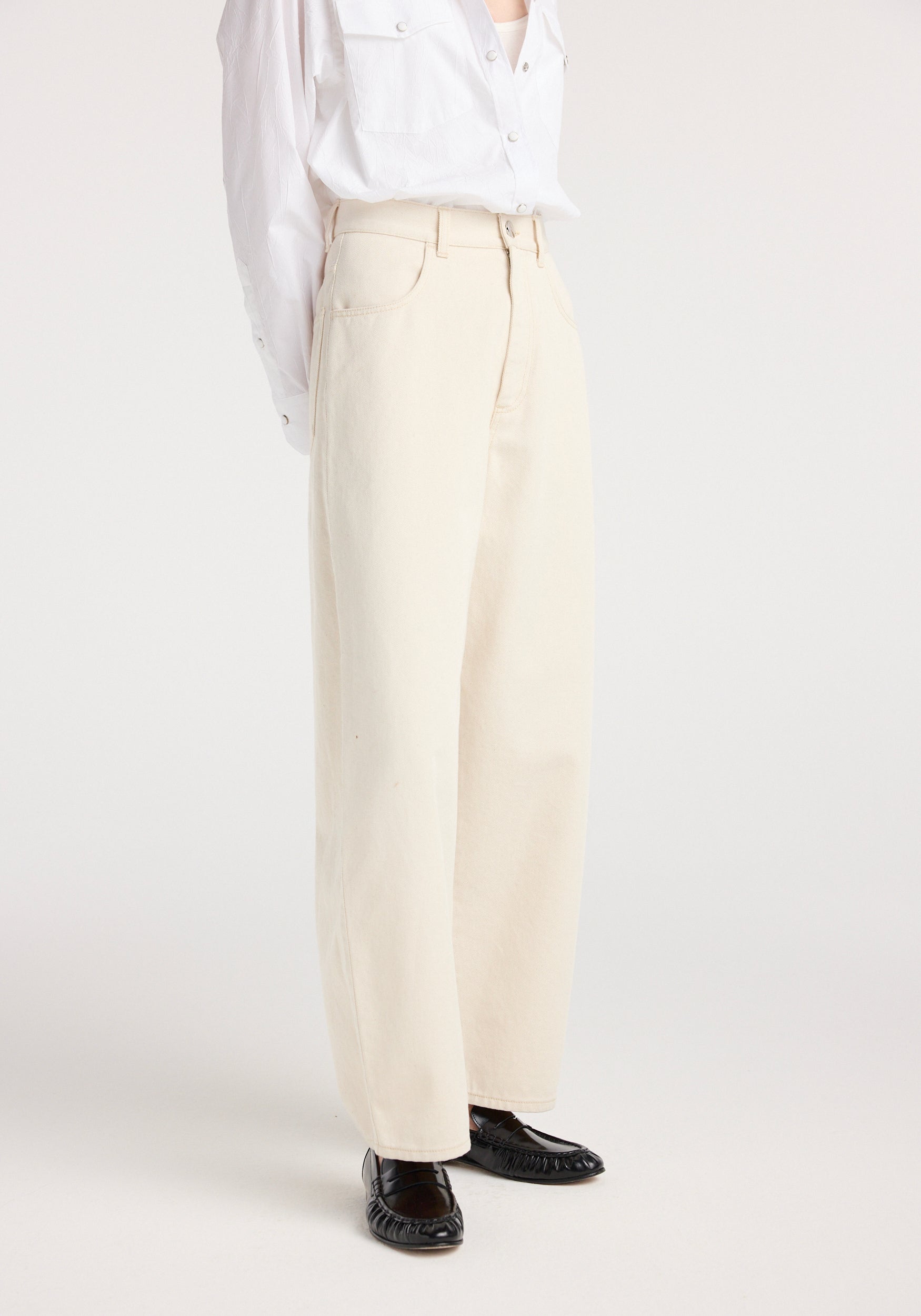 Side view of a person wearing a white shirt and beige wide-leg denim pants paired with black shoes, showcasing the "Berber - Barrel leg denim | ecru" style.