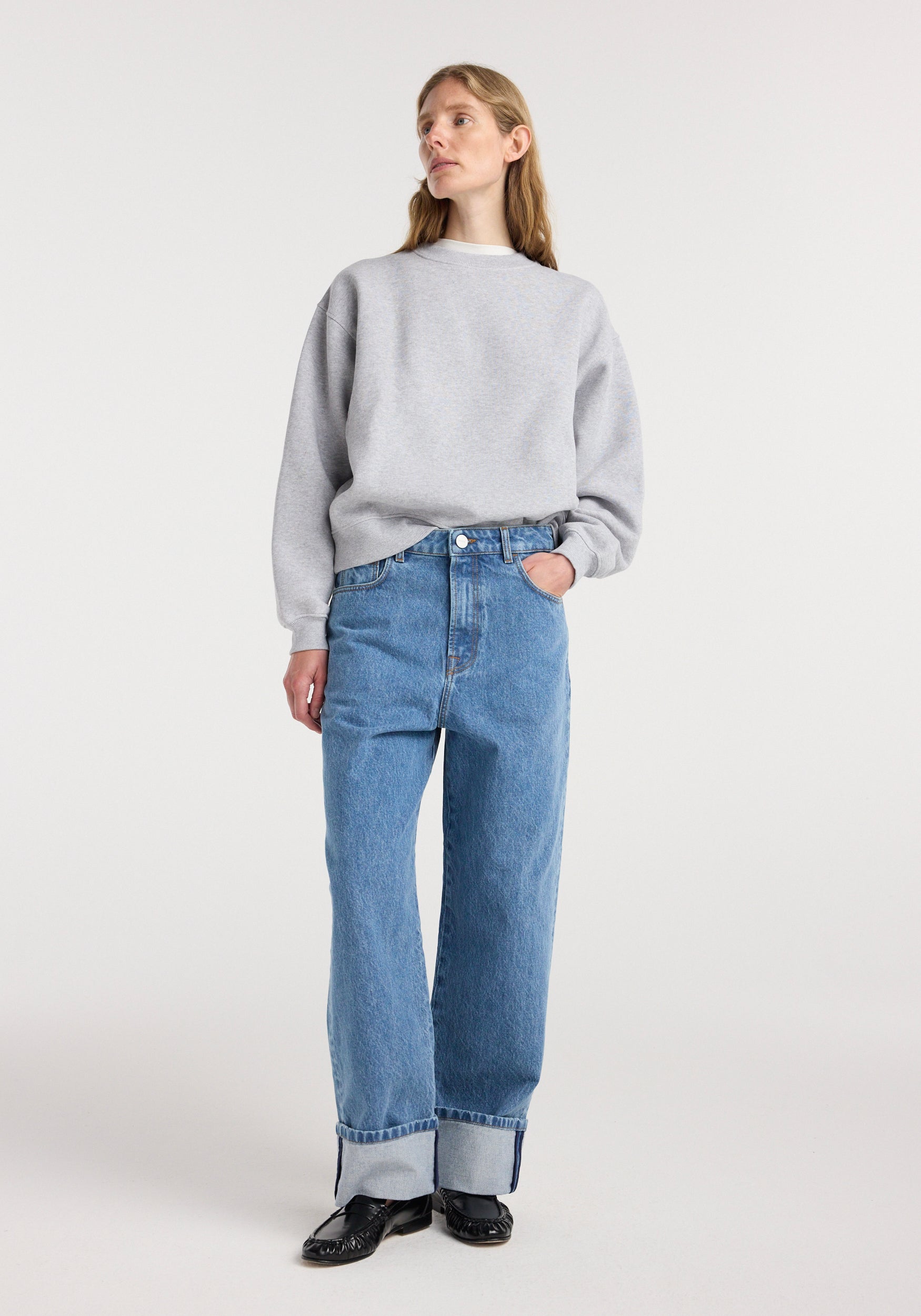 Woman wearing a gray sweatshirt paired with Rixt - Turn-up baggy denim | heritage blue jeans with cuffed hems and black shoes, standing against a plain background.