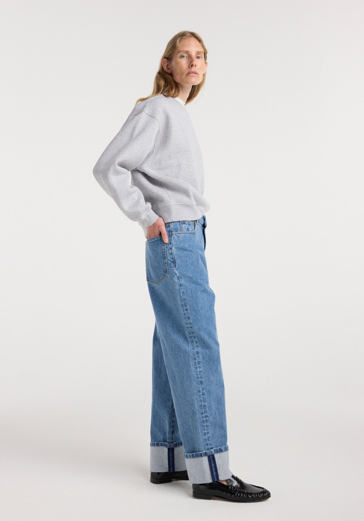 Woman wearing Rixt - Turn-up baggy denim | heritage blue with a light gray sweatshirt and black loafers, standing in profile against a white background.