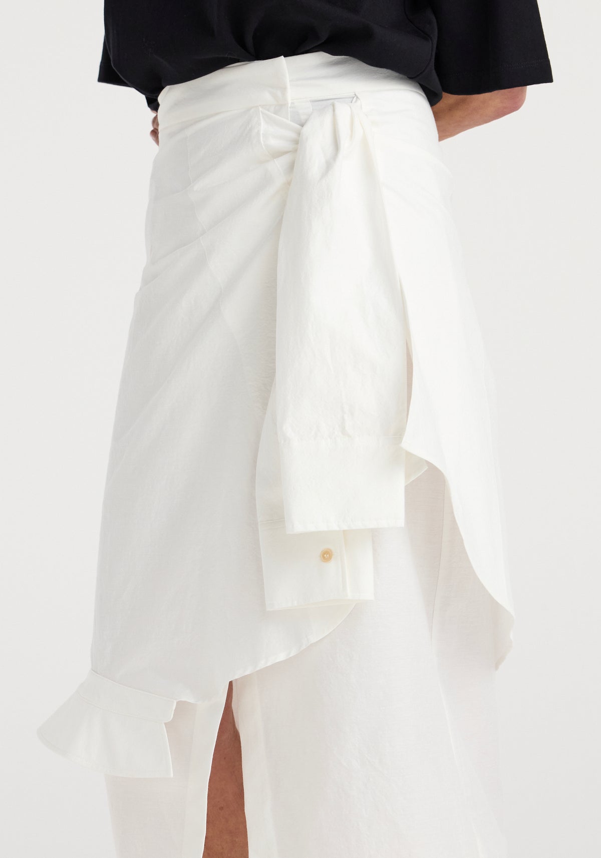 Close-up of a white shirt-wrap detailed skirt | optic white with a tied knot at the waist, featuring asymmetrical draping and lightweight fabric texture.